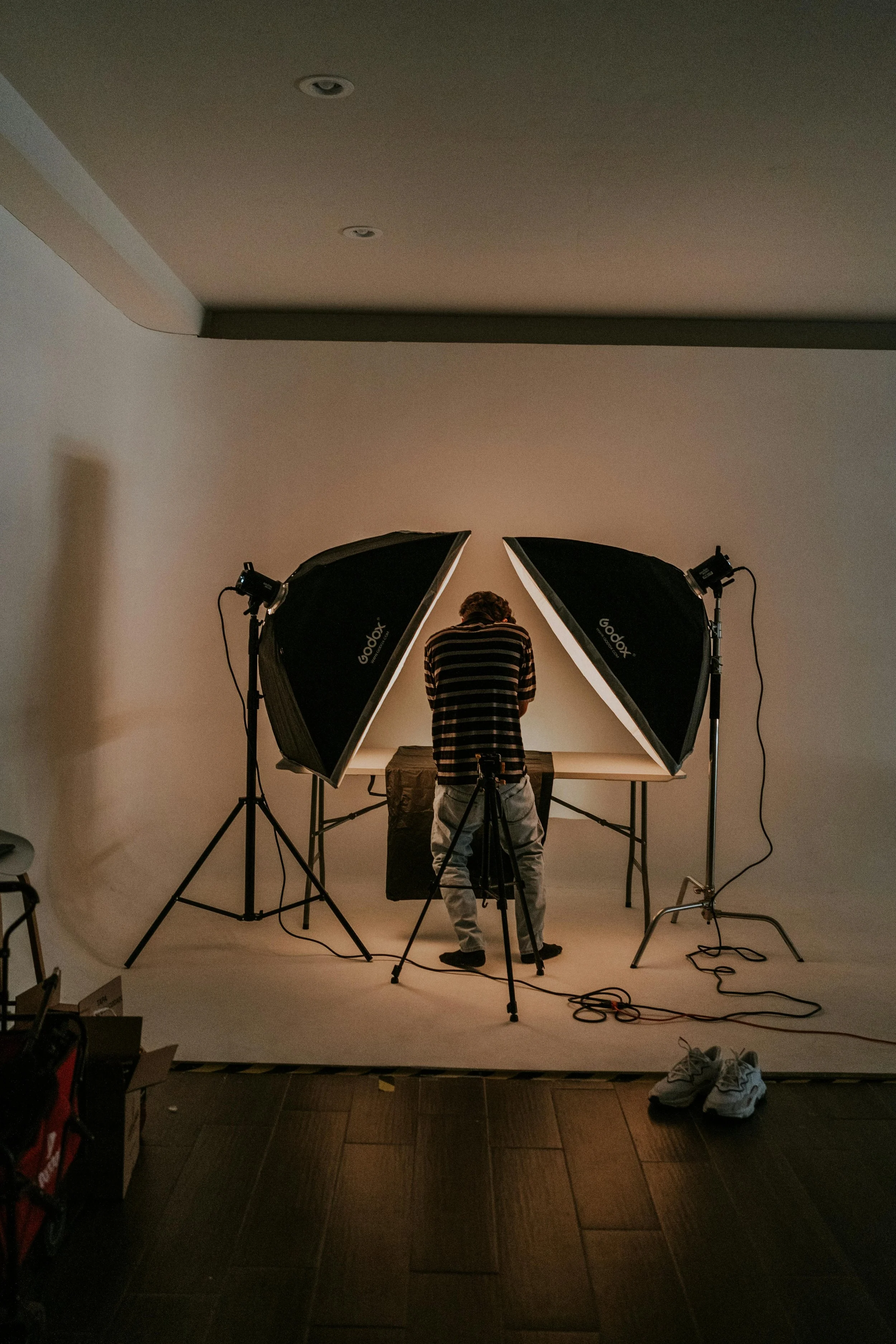 Photographer setting up studio lighting and backdrop for a photo shoot in an indoor space, with shoes on the floor.
