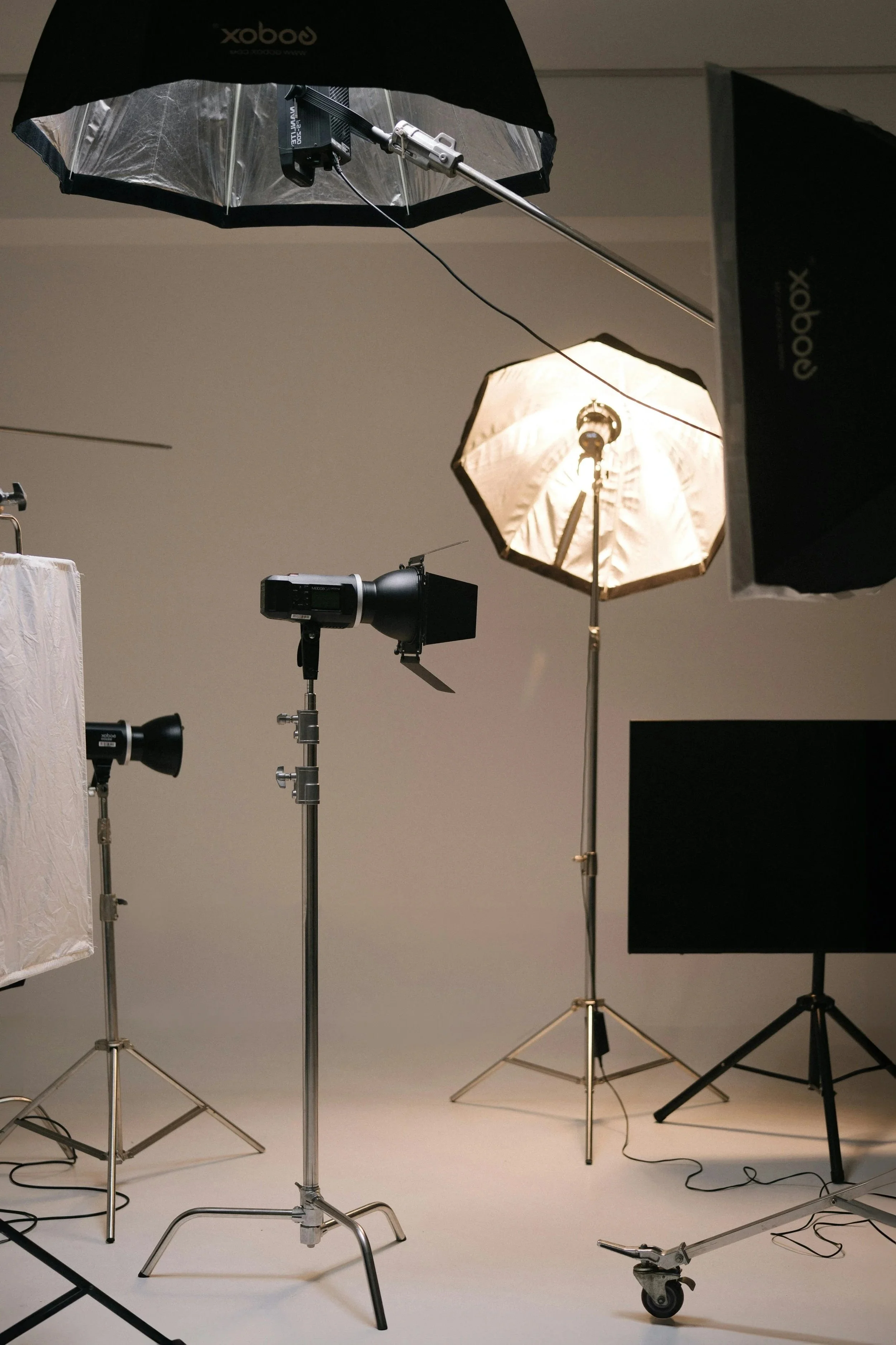 Photographic studio setup with professional lighting equipment, including softboxes, umbrella lights, and studio lights, on a plain background.