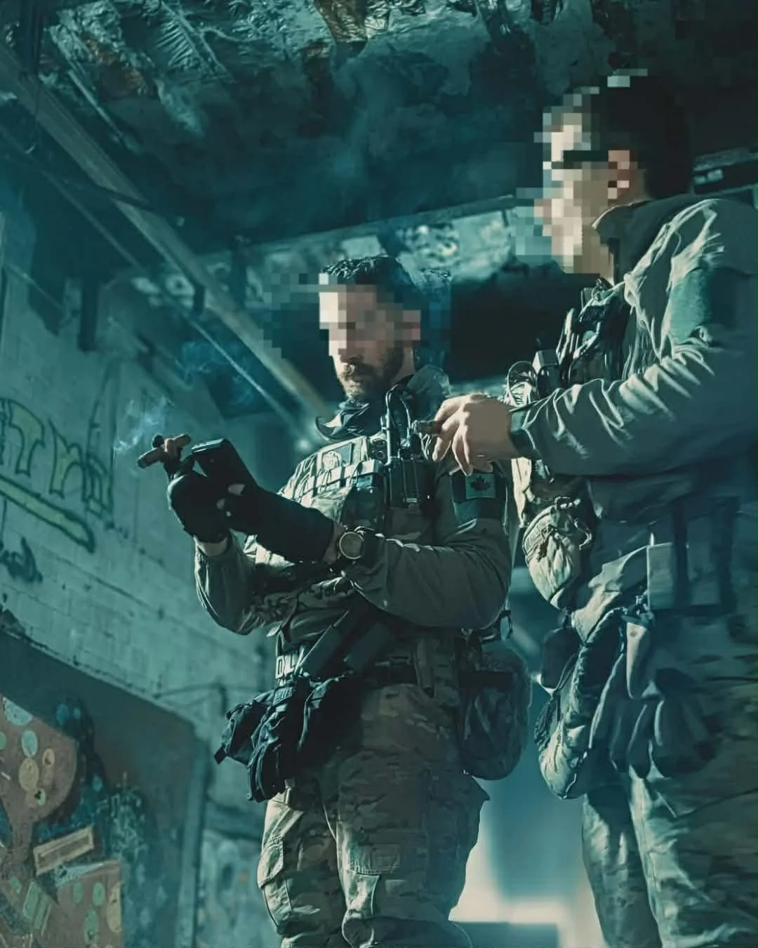Two soldiers in tactical gear standing inside a graffiti-covered building, looking at a device.