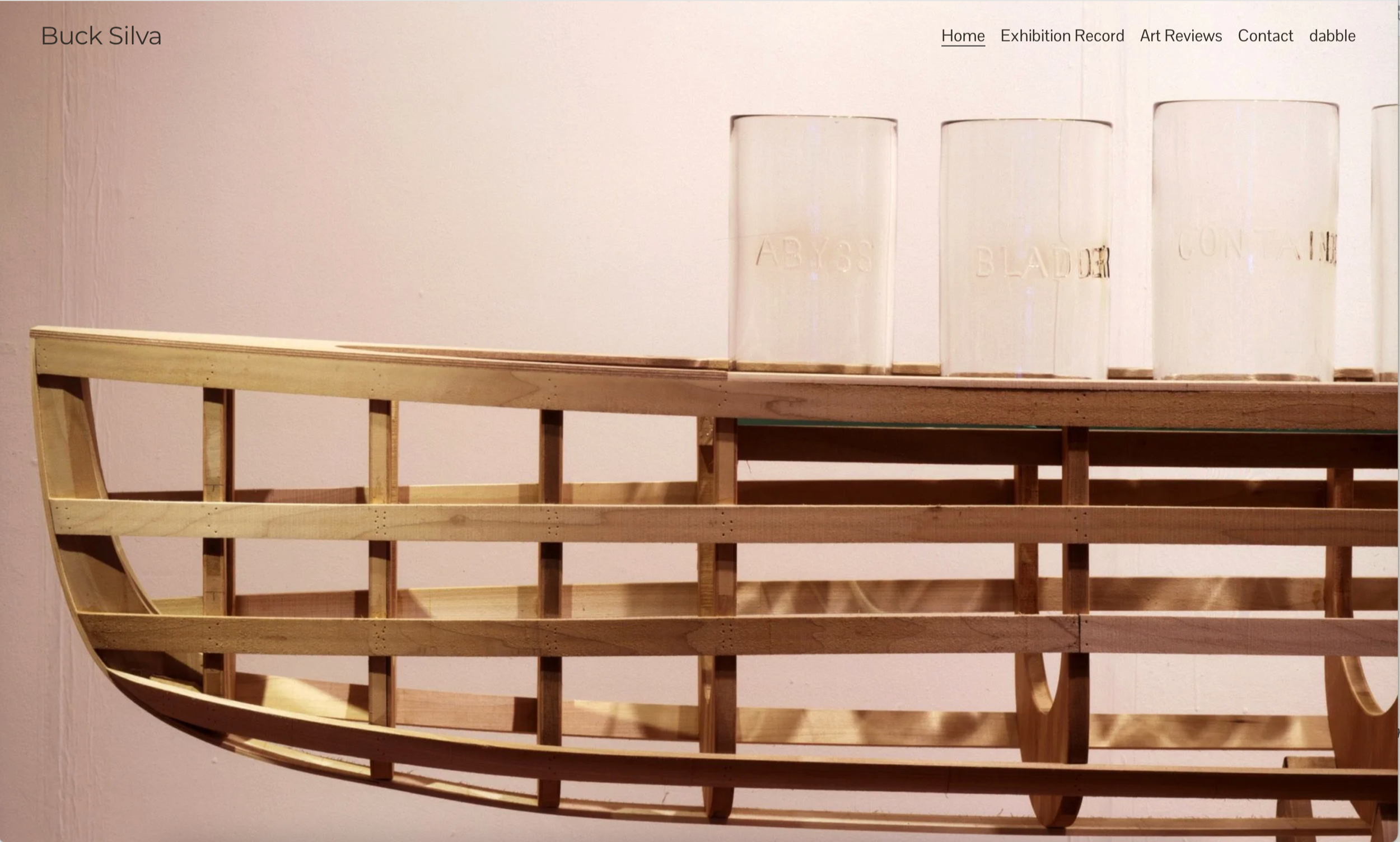 Wooden ship model under construction with a section of the hull exposed, and three clear cylindrical containers labeled 'ABYSS,' 'BLADE,' and 'CONTAIN' on a shelf above.