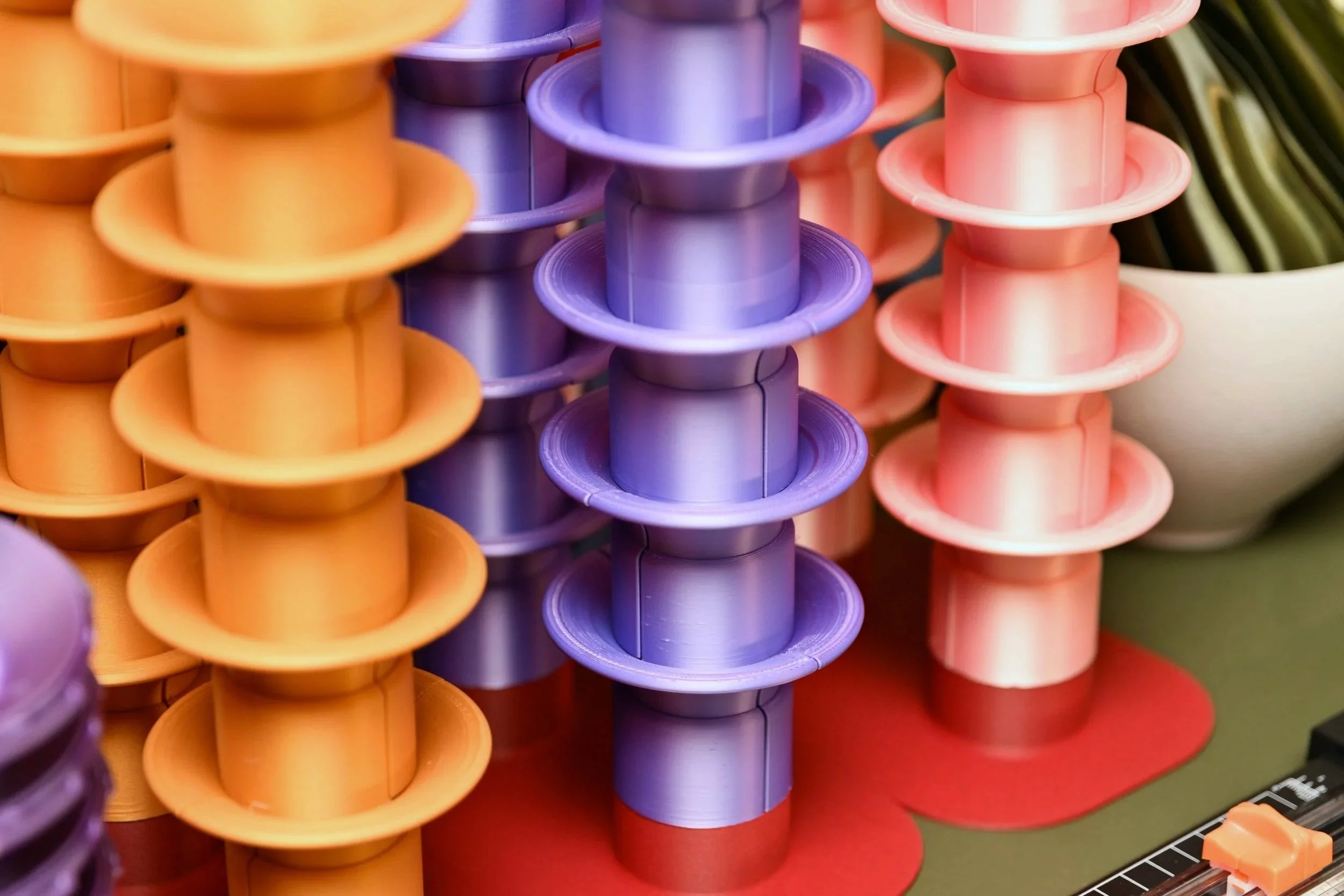 Close-up image of stacked colorful 3D printed parts, mainly purple, orange, and pink.
