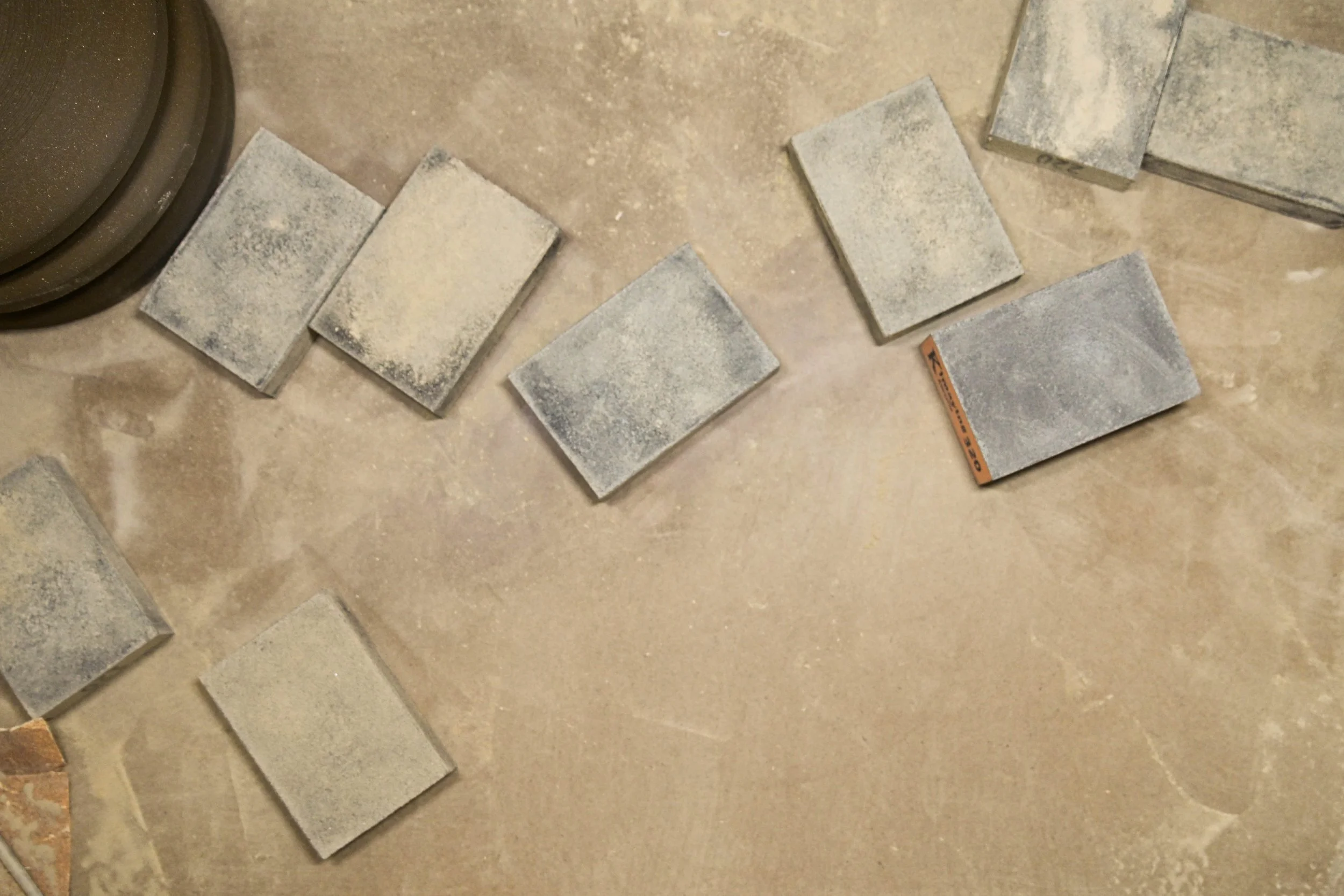 Several sanding blocks with dust and debris scattered on the floor, with some arranged and others loose.