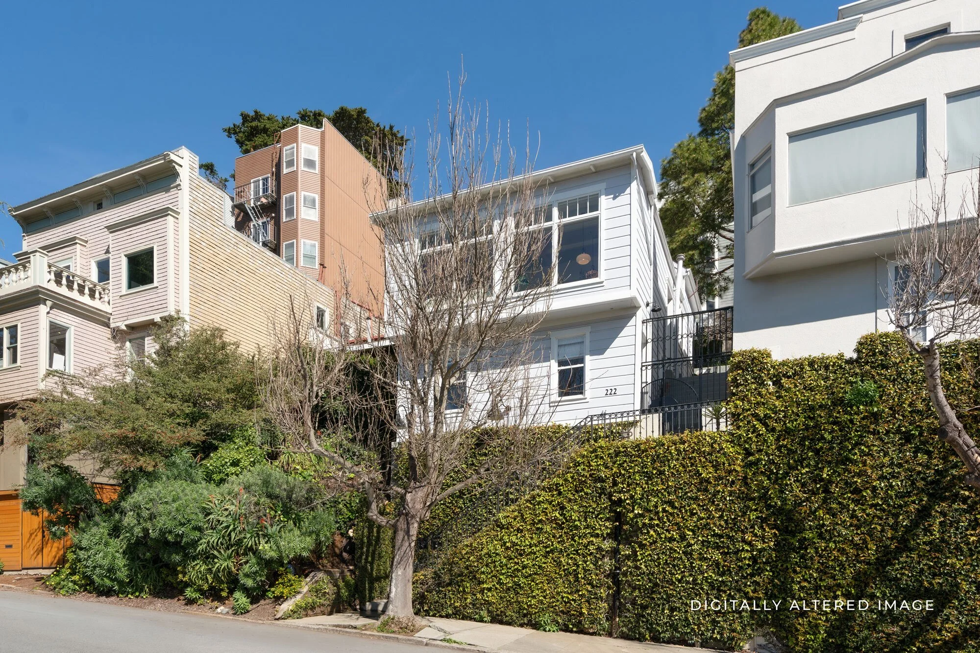 Row of colorful residential houses on a hill with trees and shrubbery in the foreground, clear blue sky.