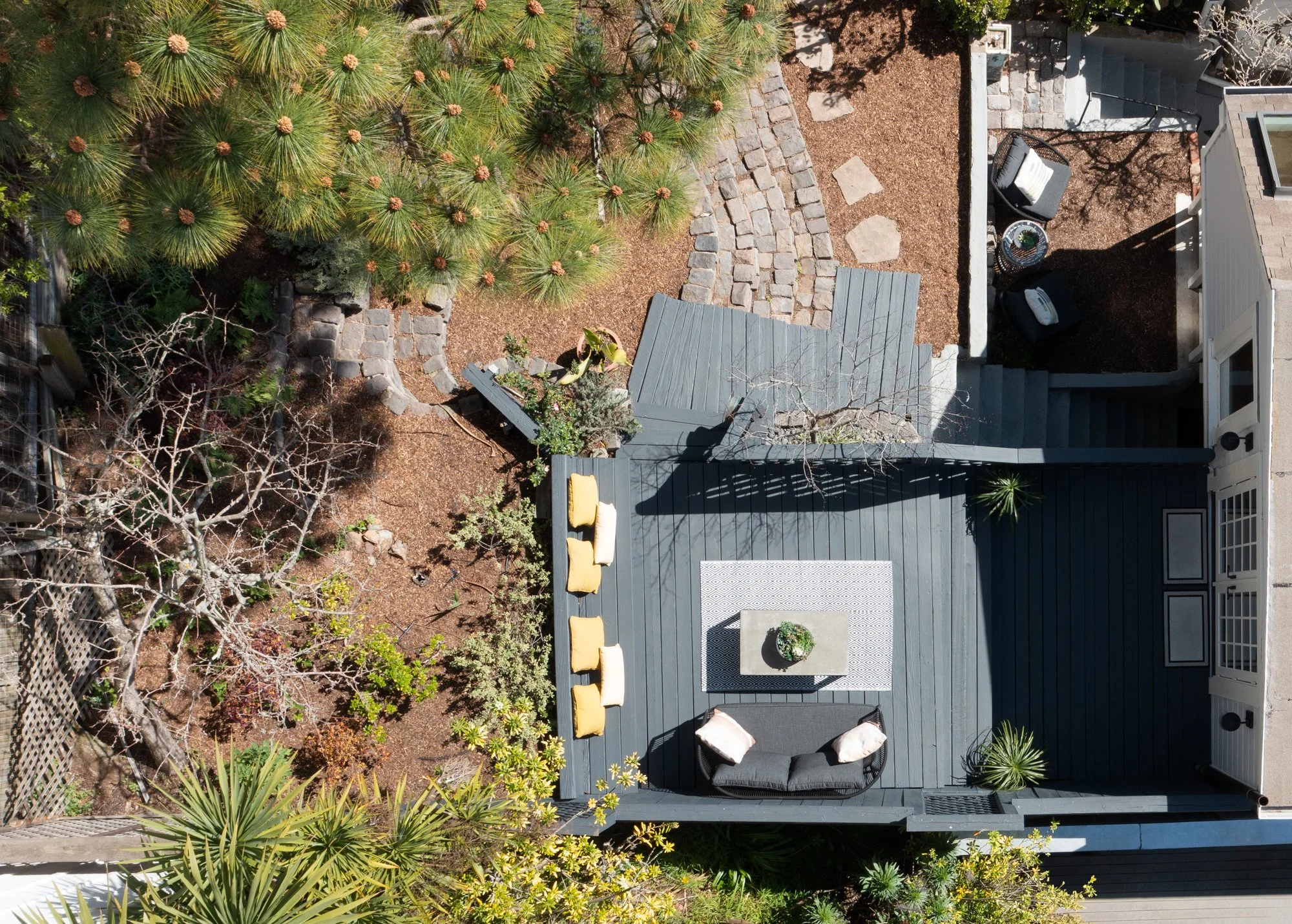 Aerial view of a backyard patio with outdoor furniture, small garden, trees, and a stone pathway