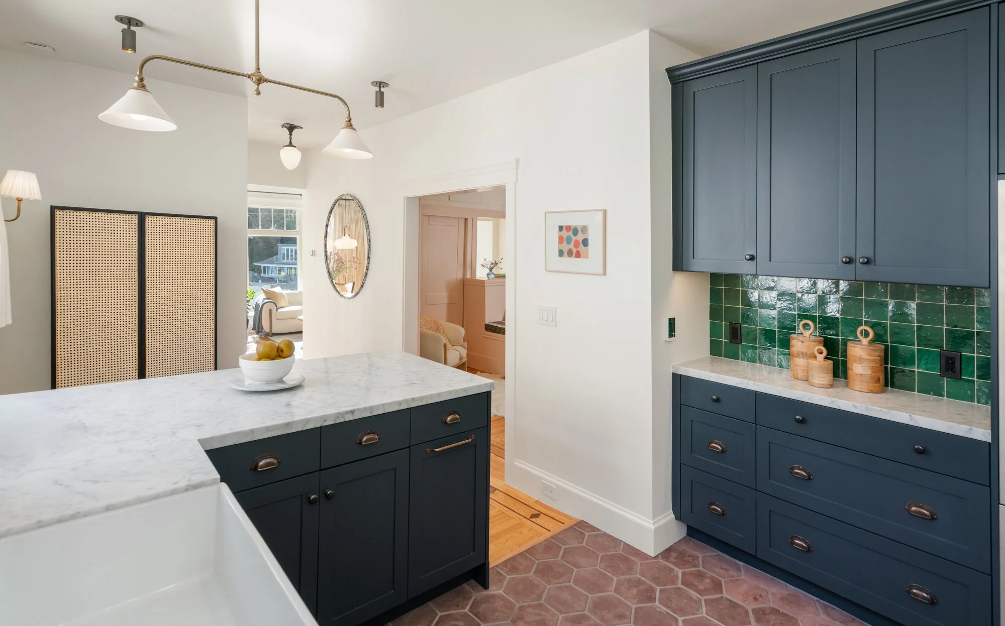 Kitchen with dark blue cabinets, green tiled backsplash, white marble countertops, and a bowl of lemons on the island