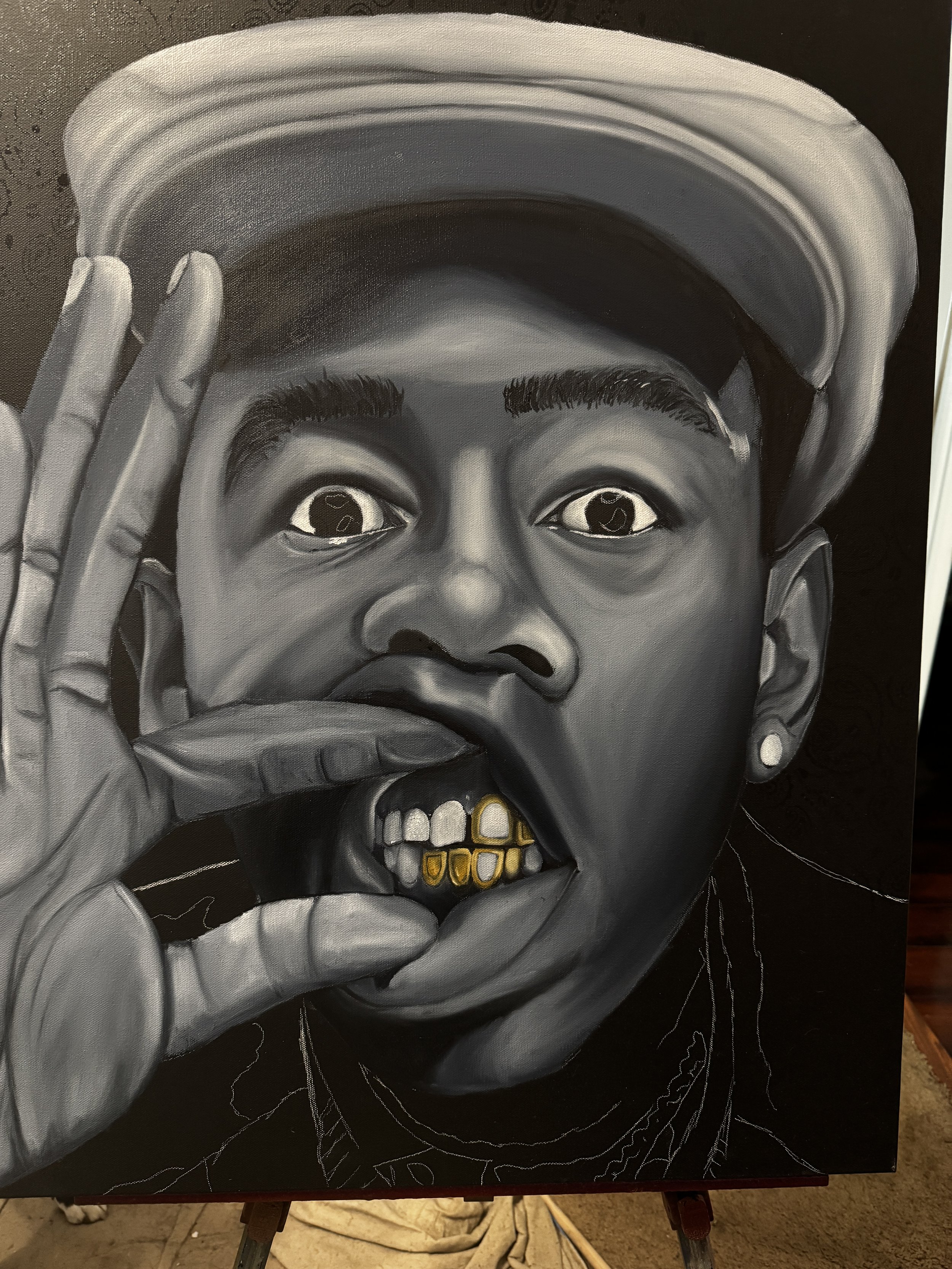 A grayscale portrait of a person wearing a hat, with wide-open eyes, holding a finger to their lips, and showing gold teeth.