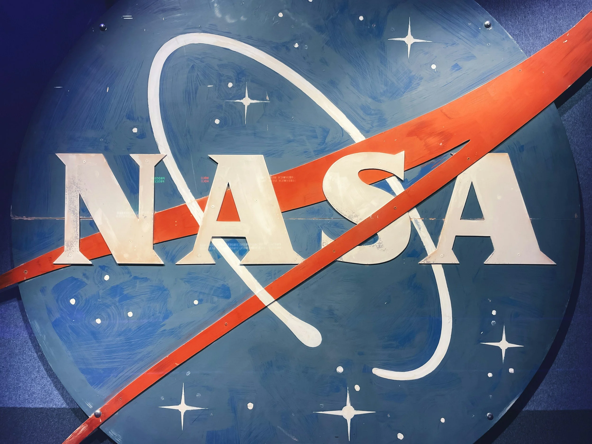 The NASA logo featuring the word 'NASA' in white letters on a blue background with stars, a white orbiting path, and an orange swoosh.