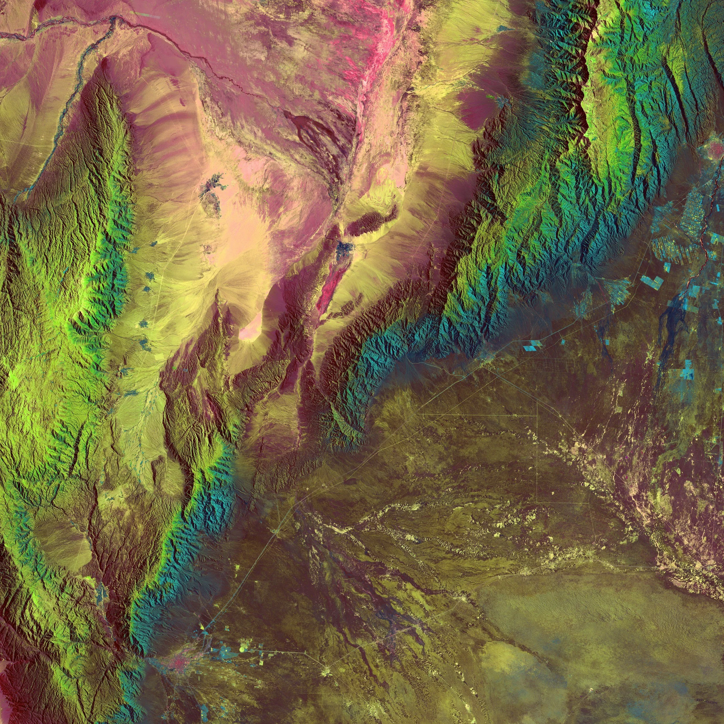 Color-enhanced satellite image of a mountainous terrain with green, yellow, pink, and blue hues indicating elevation and vegetation, along with some agricultural patches and river networks.