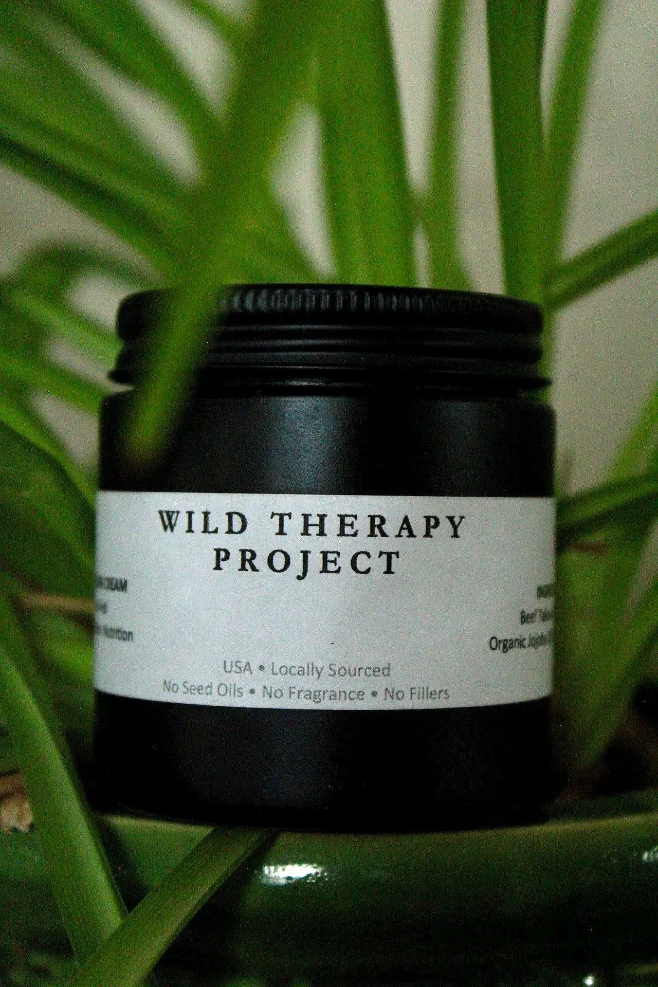 A black Jar labeled 'Wild Therapy Project' surrounded by green plant leaves.