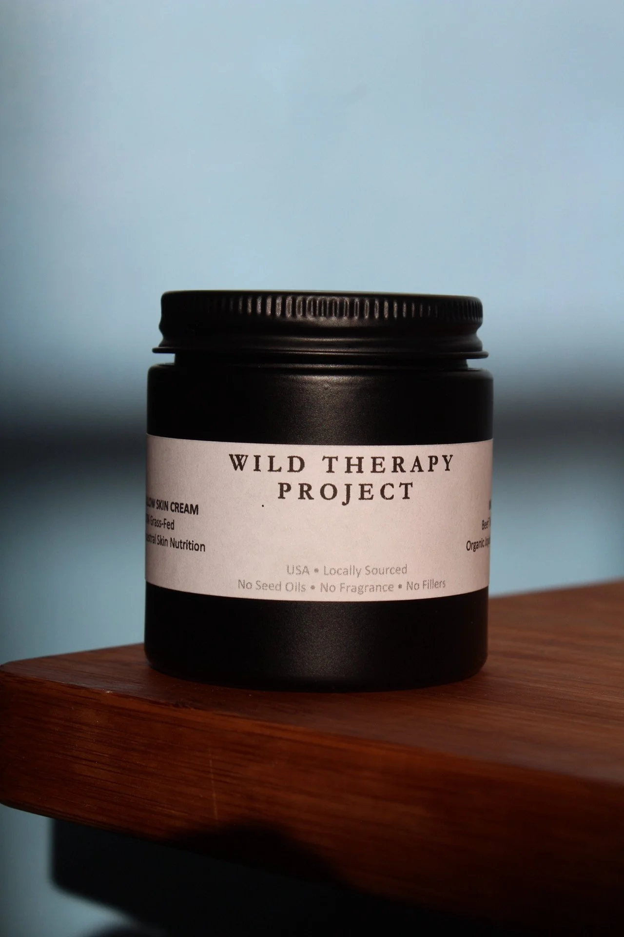 A black jar labeled "Wild Therapy Project" sitting on a wooden surface against a soft blue background.