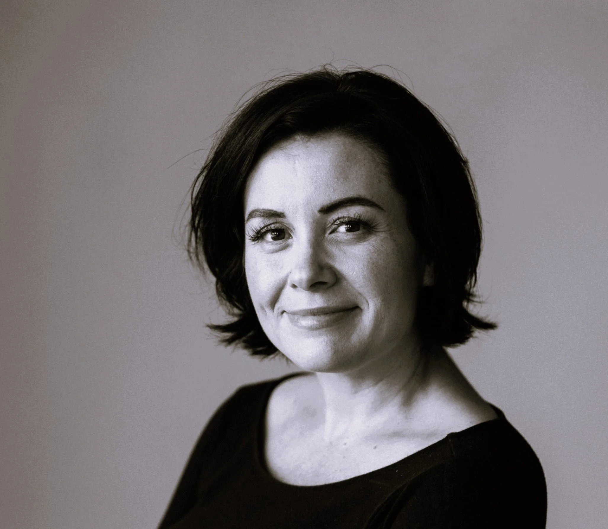 Black and white portrait of a woman with short dark hair, smiling softly, wearing a black top, against a plain background.