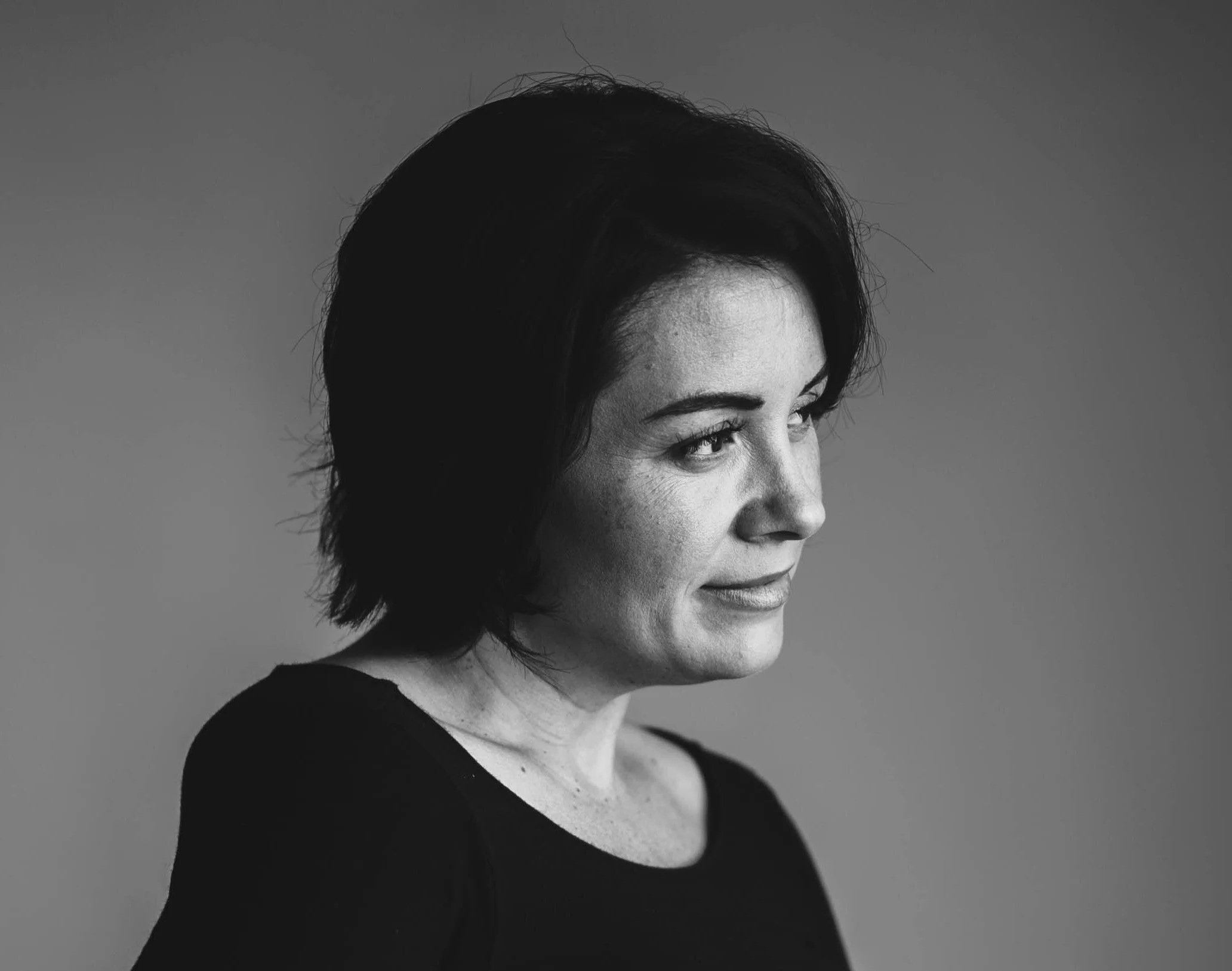 Black and white portrait of a woman with short dark hair, looking to the right with a slight smile, wearing a black top, against a plain background.