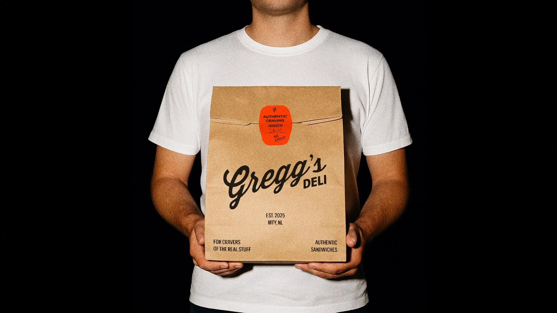 Person in a white T-shirt holding a Greg's Deli takeout bag with a red sticker that reads 'Authentic craving.'