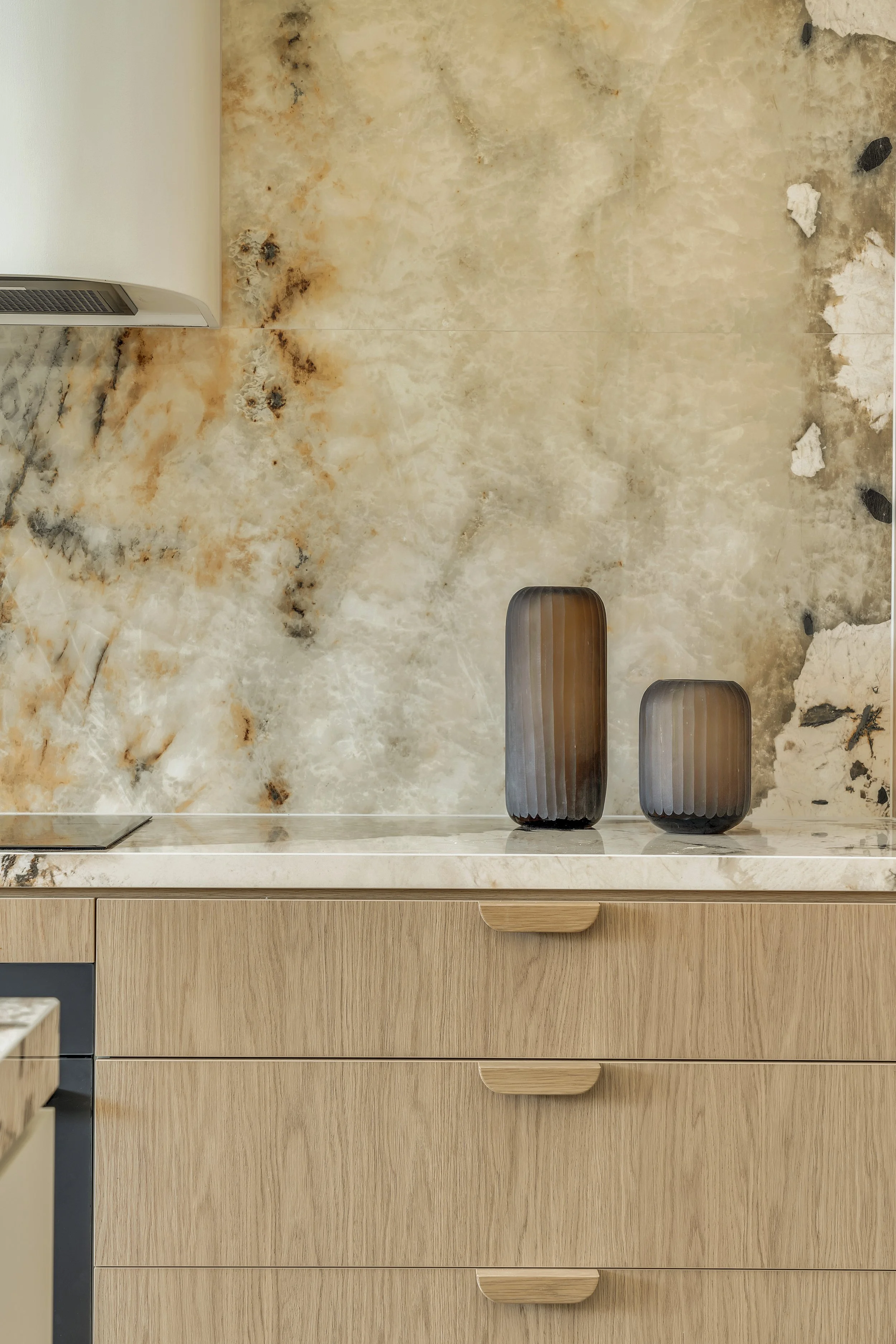 A kitchen countertop with two brown vases on a beige marble backsplash and wooden cabinets below.