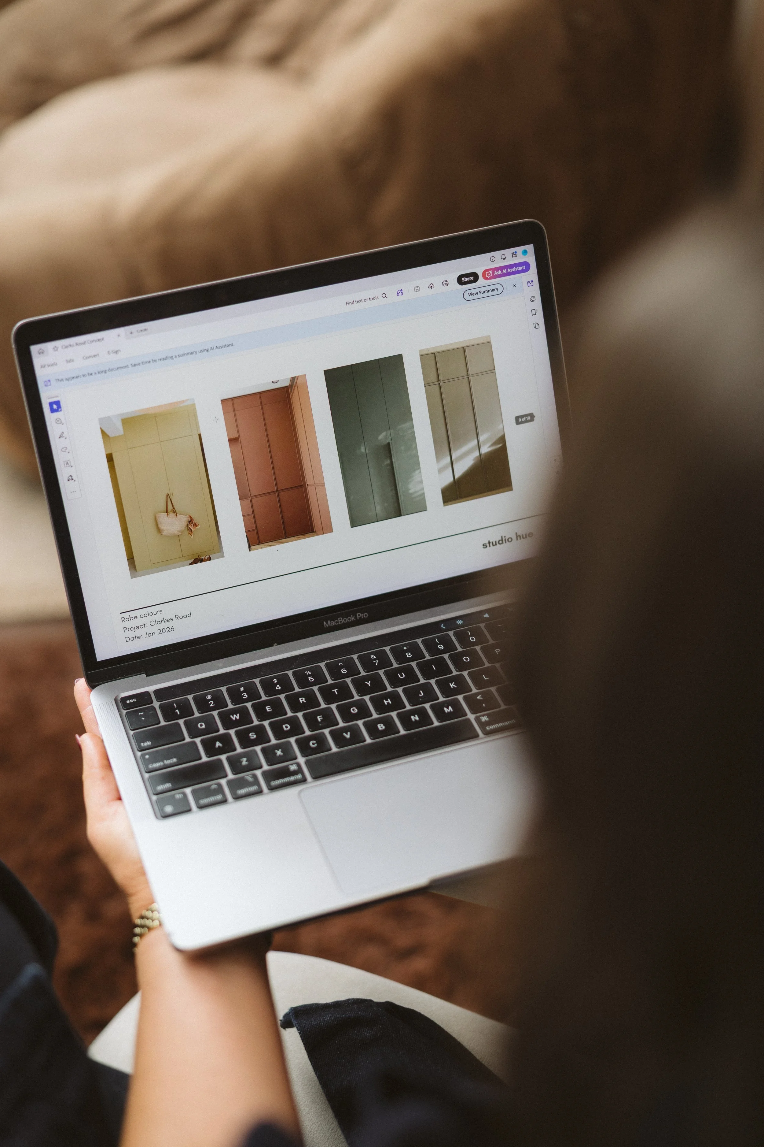 A person holding a MacBook Pro laptop, browsing images of built-in wardrobes on the screen, with their left hand supporting the bottom of the laptop and wearing a bracelet.