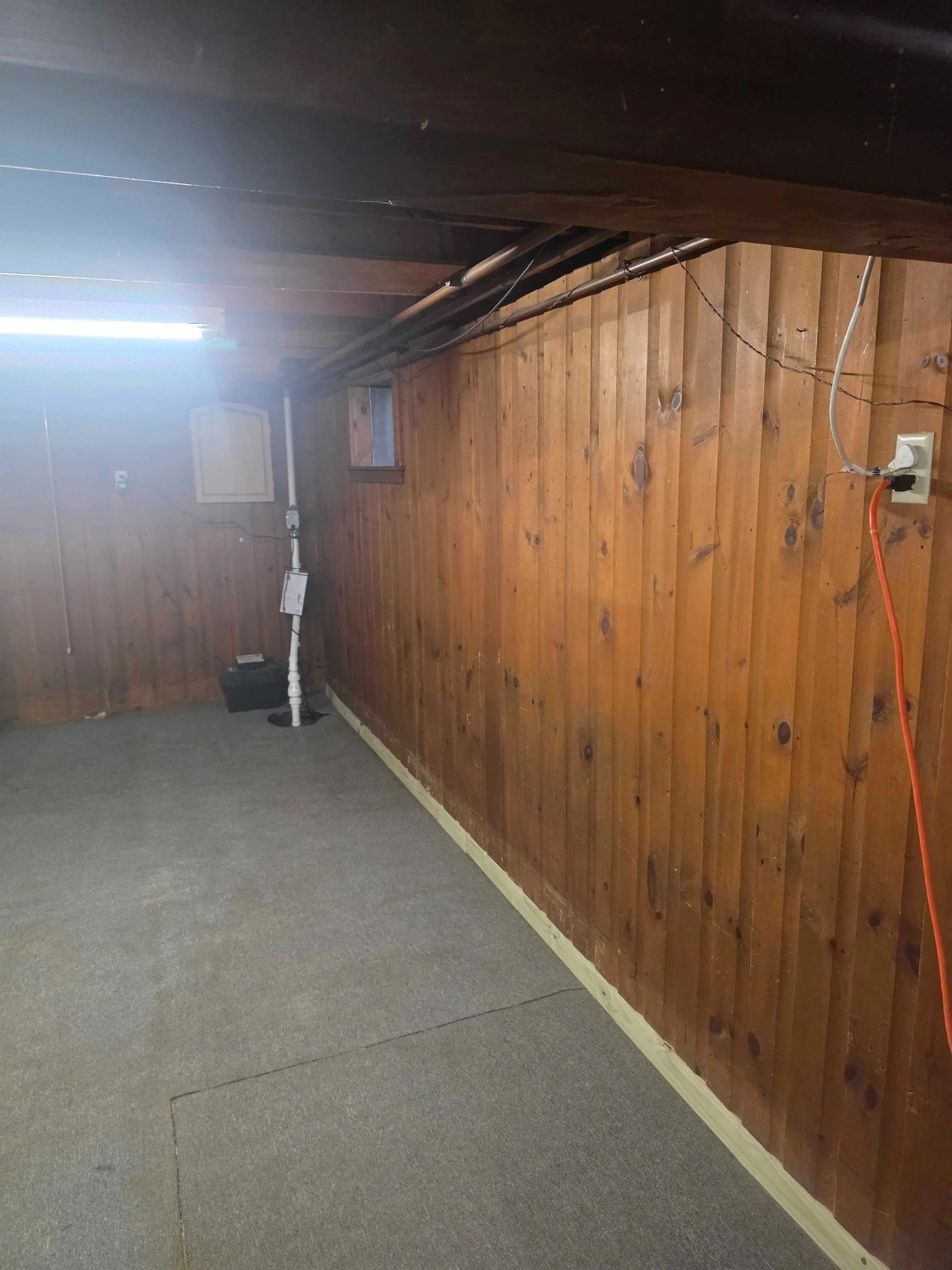 Finished wood-panel basement after waterproofing system installation and wall reassembly.