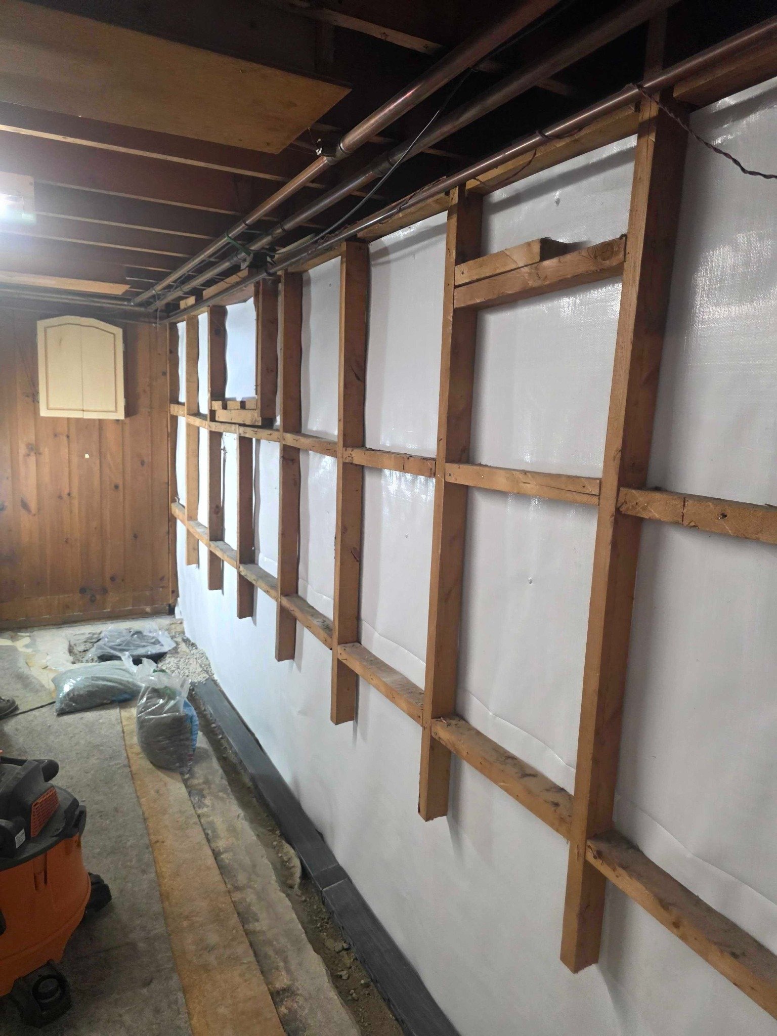 Exposed basement wall framing and vapor barrier after wood panel demolition in Manchester, NH.