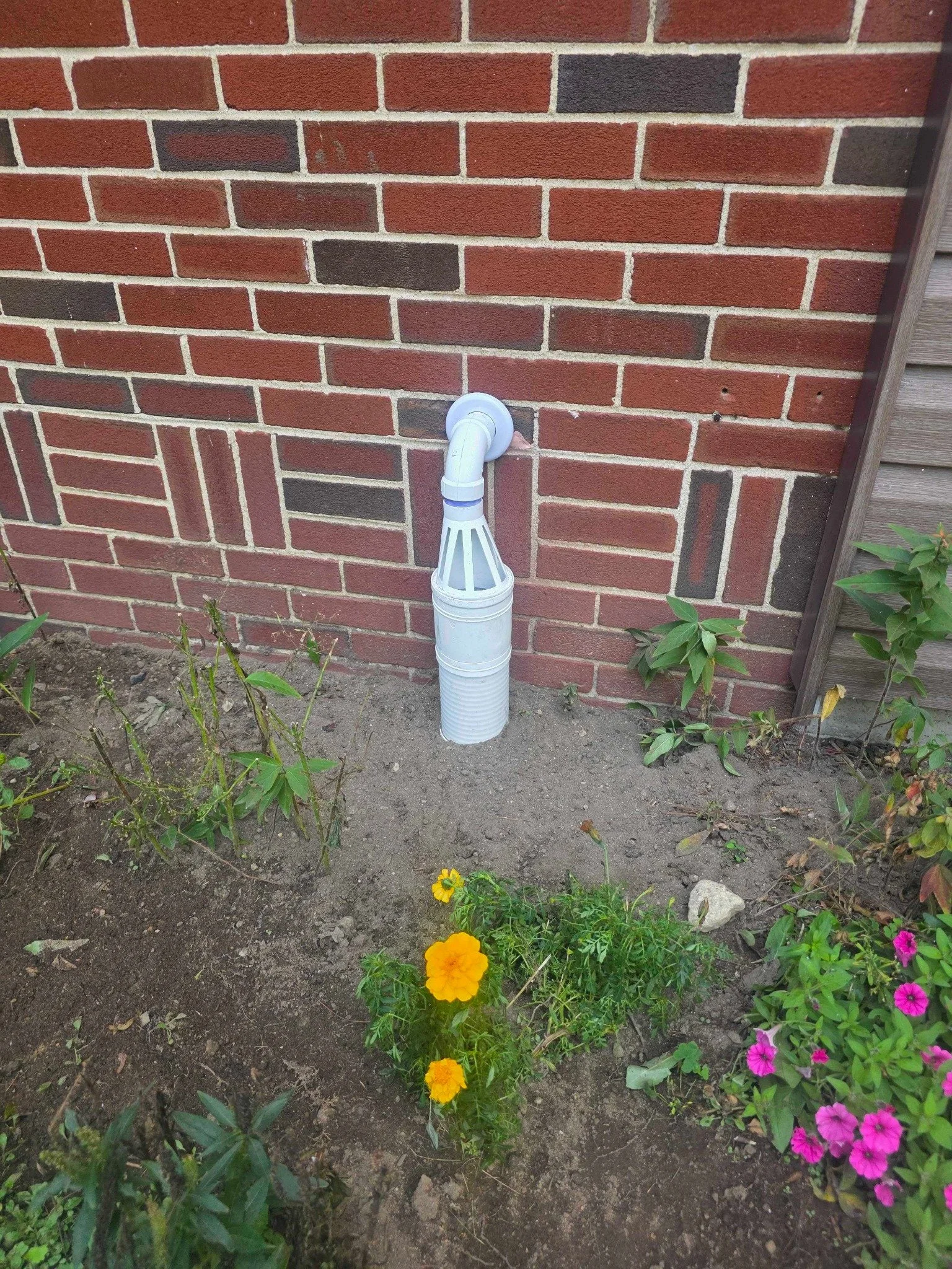 Exterior sump pump discharge outlet installed through a brick foundation wall in Manchester, NH.