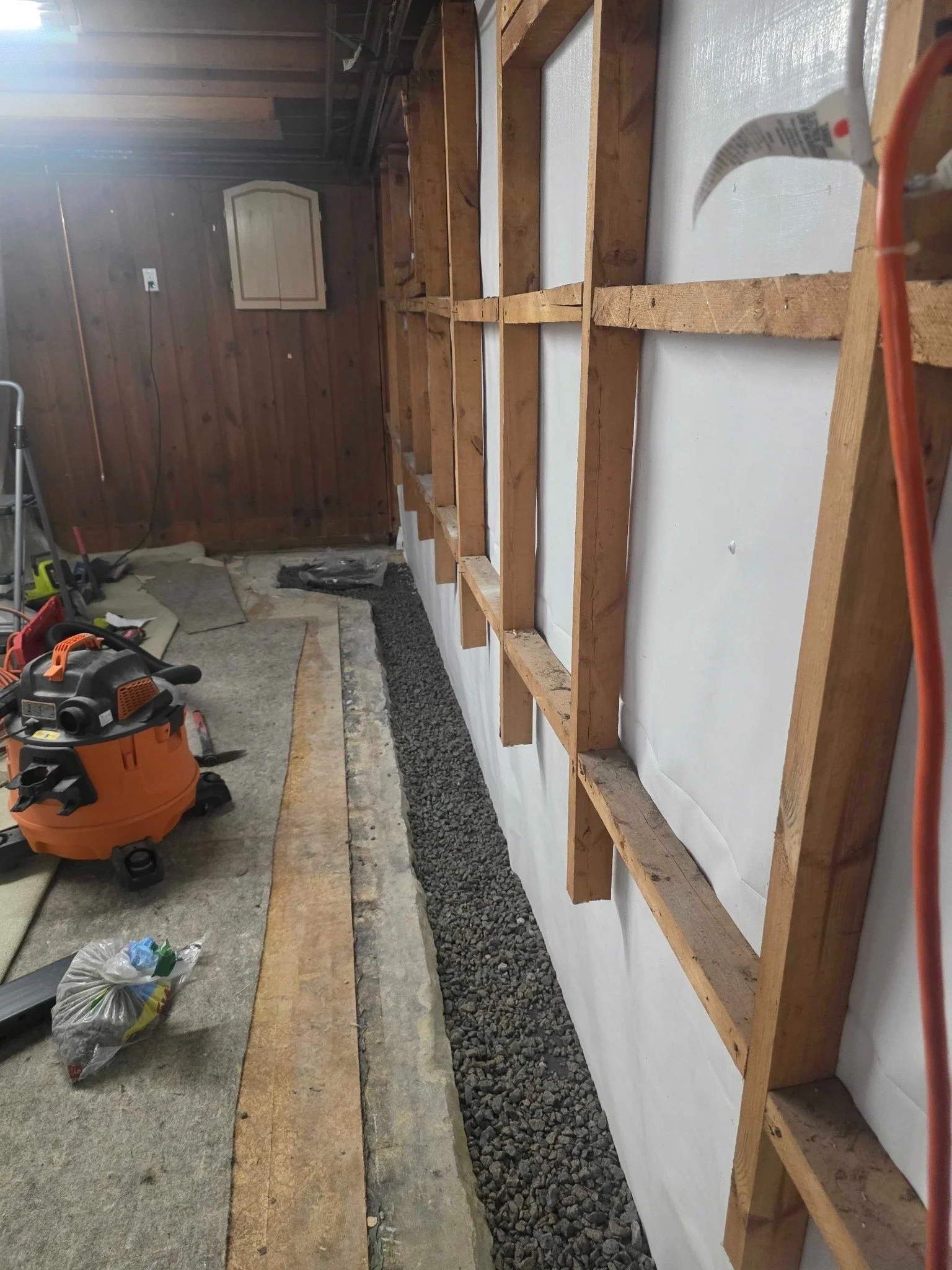 Tools beside the stone-filled basement drainage trench and exposed wall framing.