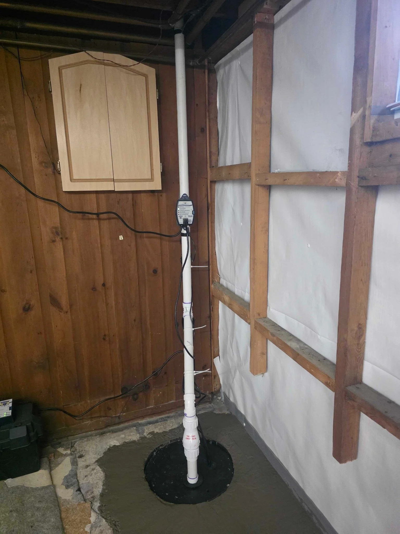 Sump discharge piping installed beside repaired basement framing and wall vapor barrier.