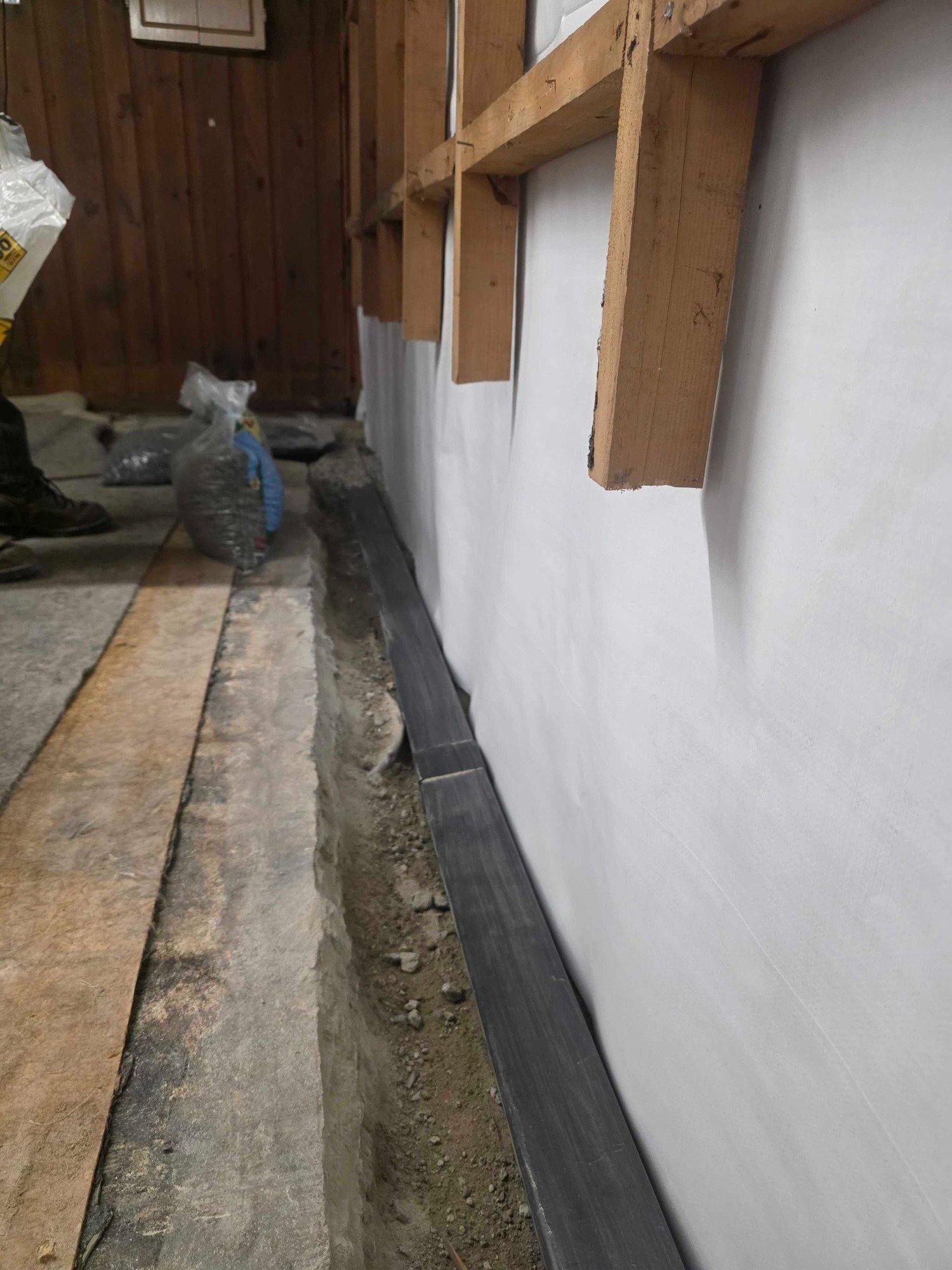 Open slab-edge drainage trench and wall vapor barrier during a Manchester New Hampshire basement waterproofing project