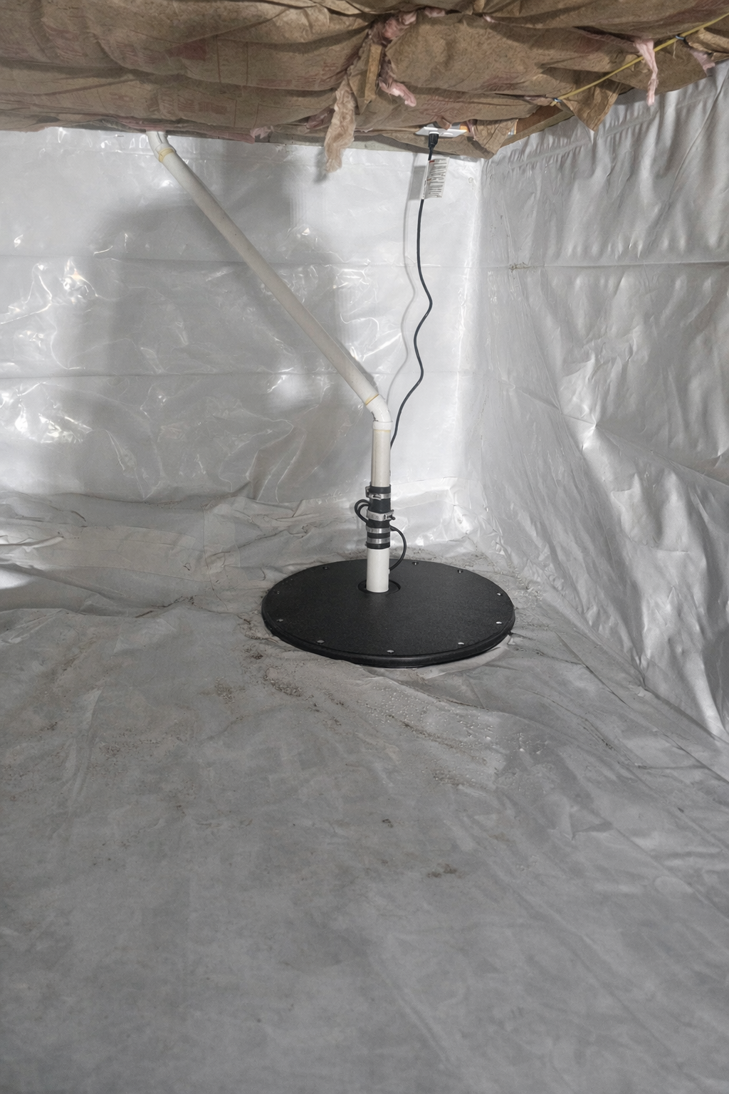 A black round disc with a pipe and electrical cord inside a room lined with reflective insulation material.