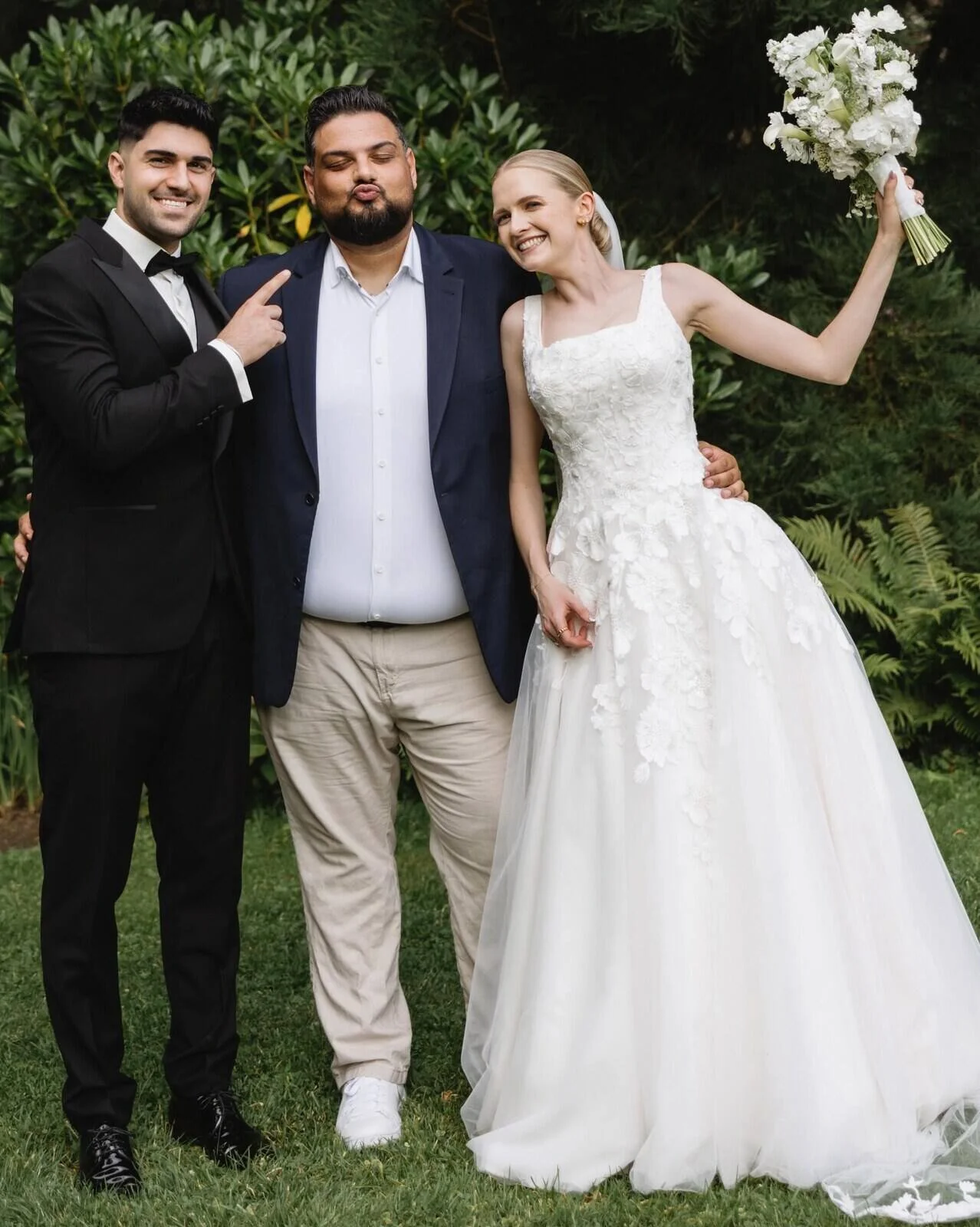 Der freie Trauredner Pedi mit seinem Brautpaar nach einer Trauung. Bräutigam im schwarzen Smoking und lächelnd, Braut strahlend in einem Brautkleid mit ihrem Brautstrauß.