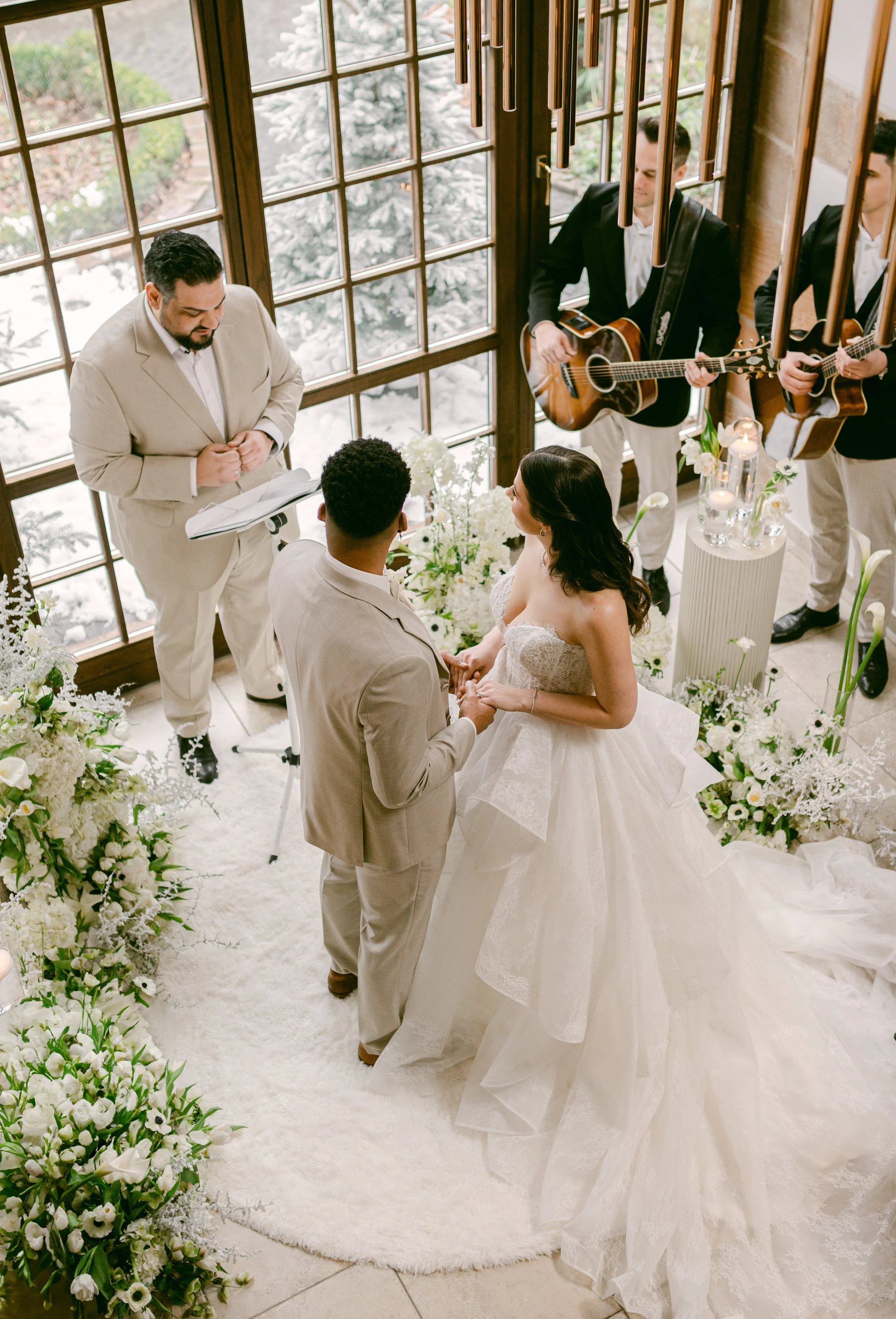 Hochzeitspaar bei der freier Trauung mit dem freien Trauredner Pedi. Trauung mit Musikern im Hintergrund, im Raum mit großen Fenstern und winterlichem Außenbereich.