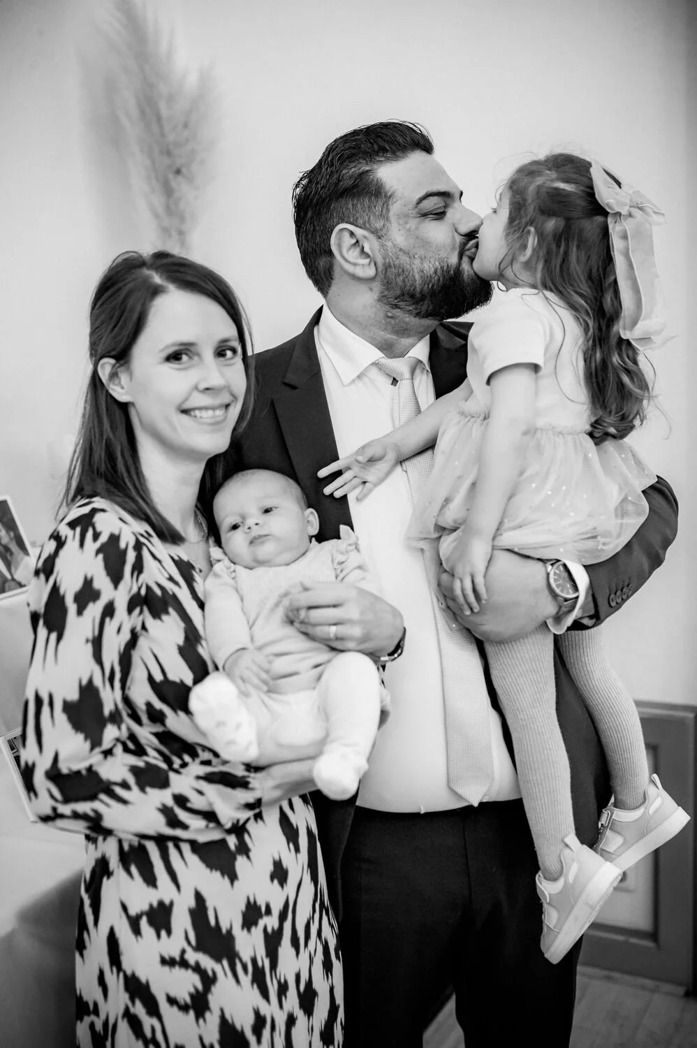 Der freie Trauredner Pedi mit seiner glücklichen Familie, die einen Kuss teilt, während eine Frau ein Baby hält, und ein weiteres Kind auf dem Arm des Mannes sitzt.