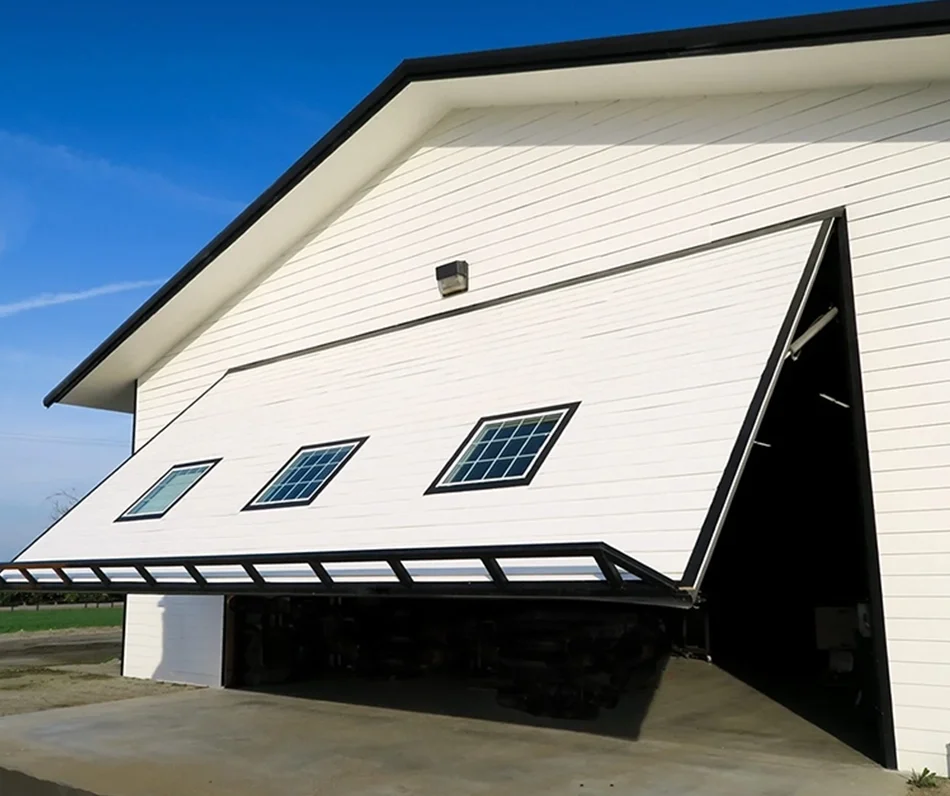 A house with a garage door that opens at an angle, resembling a barn door, revealing three small windows on the door. The house is white with black trim, and the sky is clear and blue.
