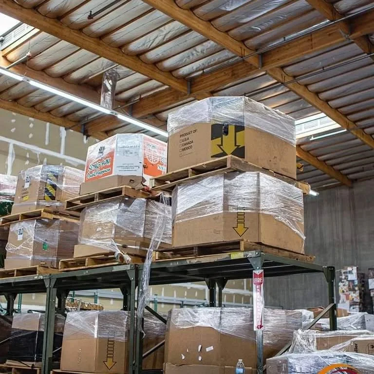 Pallets with boxes and packaging material stored on industrial warehouse shelves.
