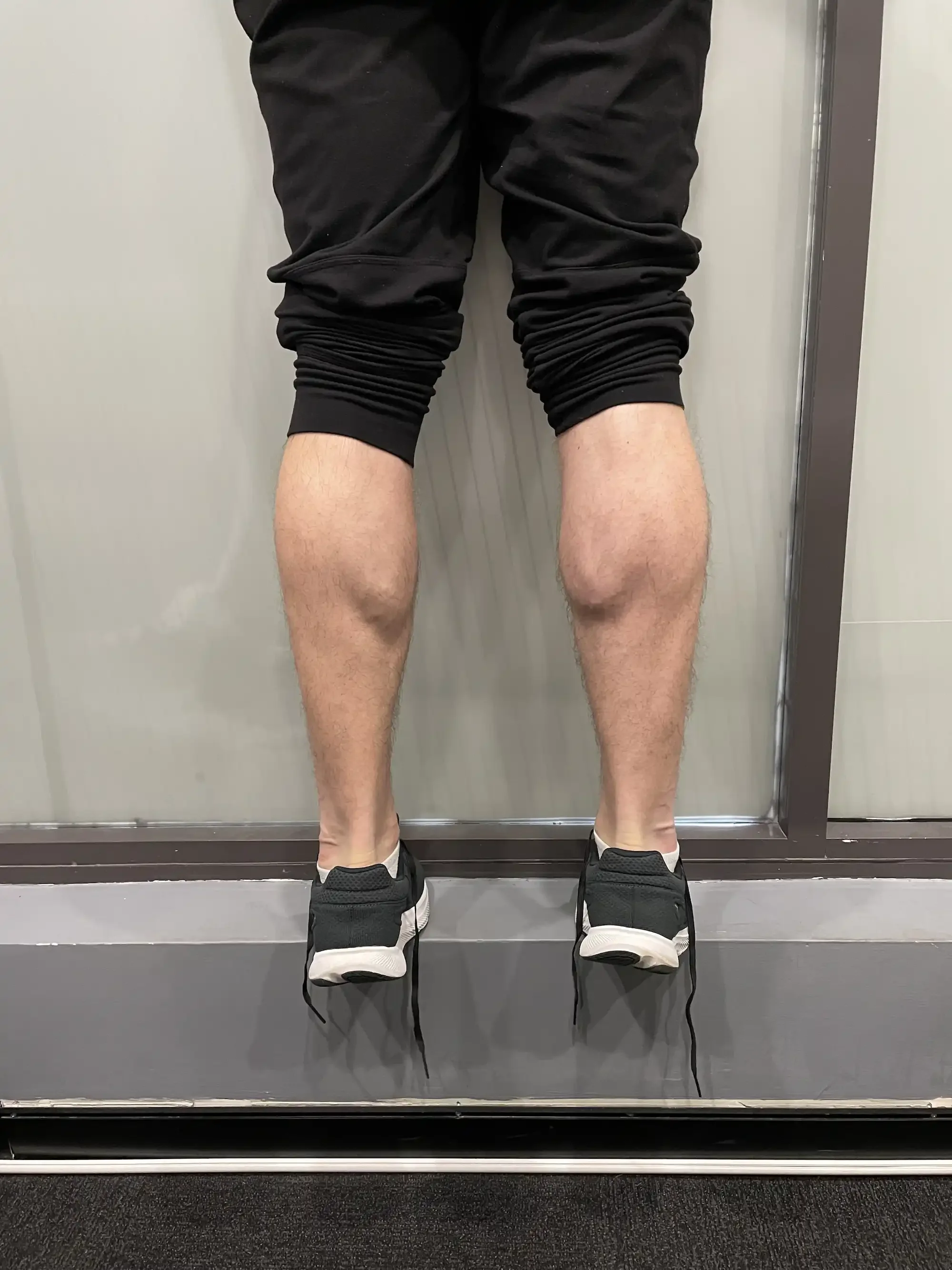 A person wearing black shorts and sneakers, standing in an elevator with their legs visible.