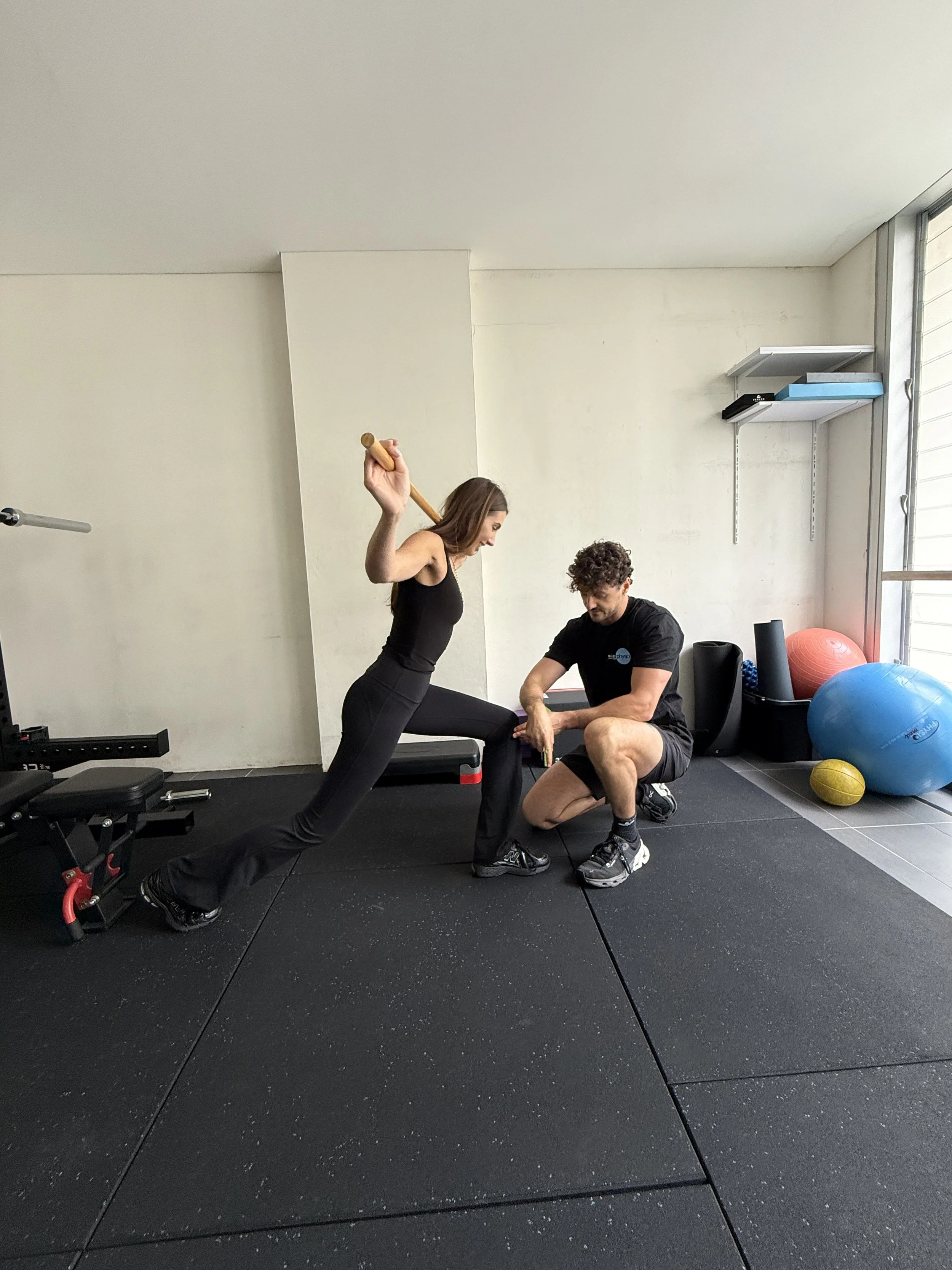 A woman with straight dark hair performing a lunge with guidance from expert physiotherapist to improve knee function and reduce pain