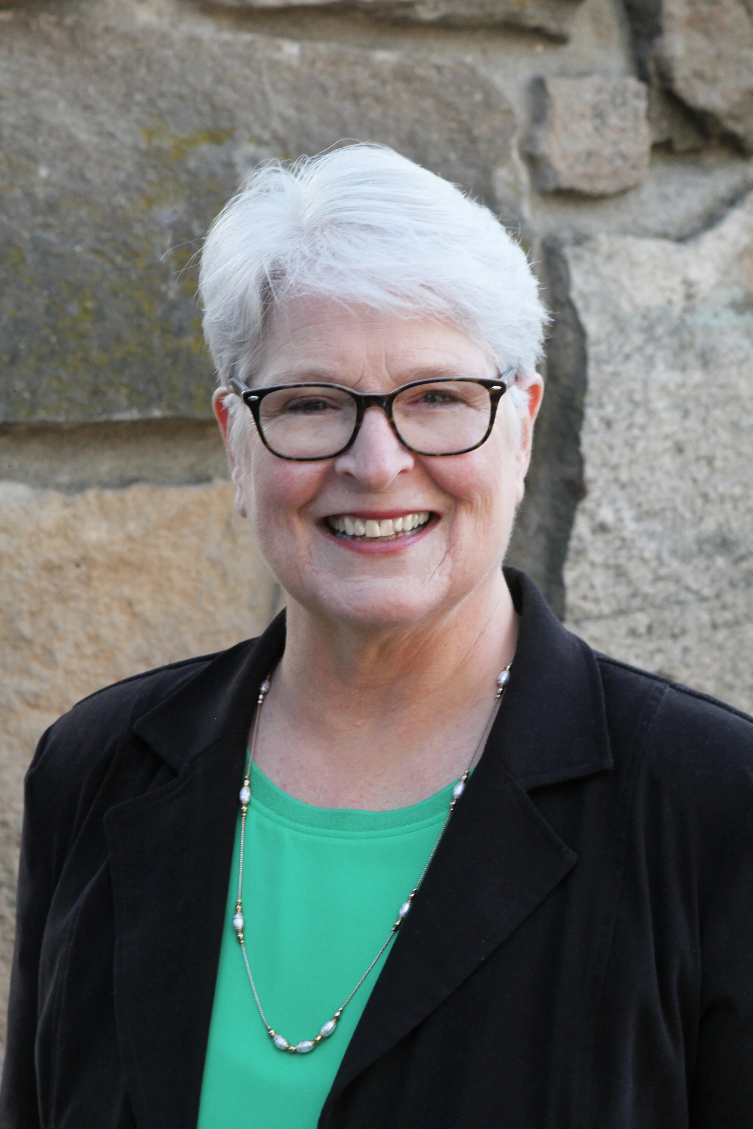 A woman with white hair and tortoise shell glasses smiling.