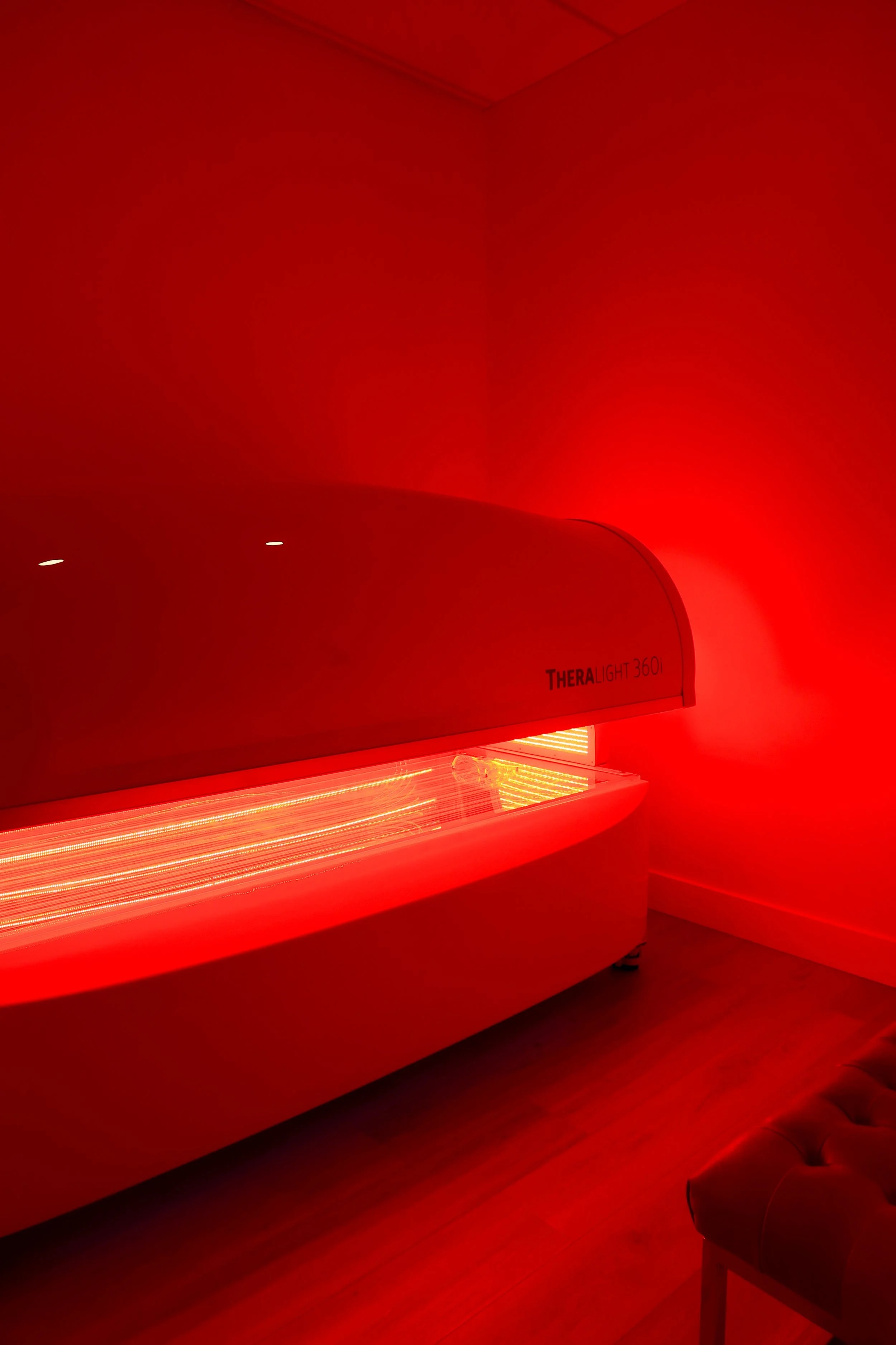 A red tanning bed labeled 'TheaLight 360' in a room illuminated by red light.