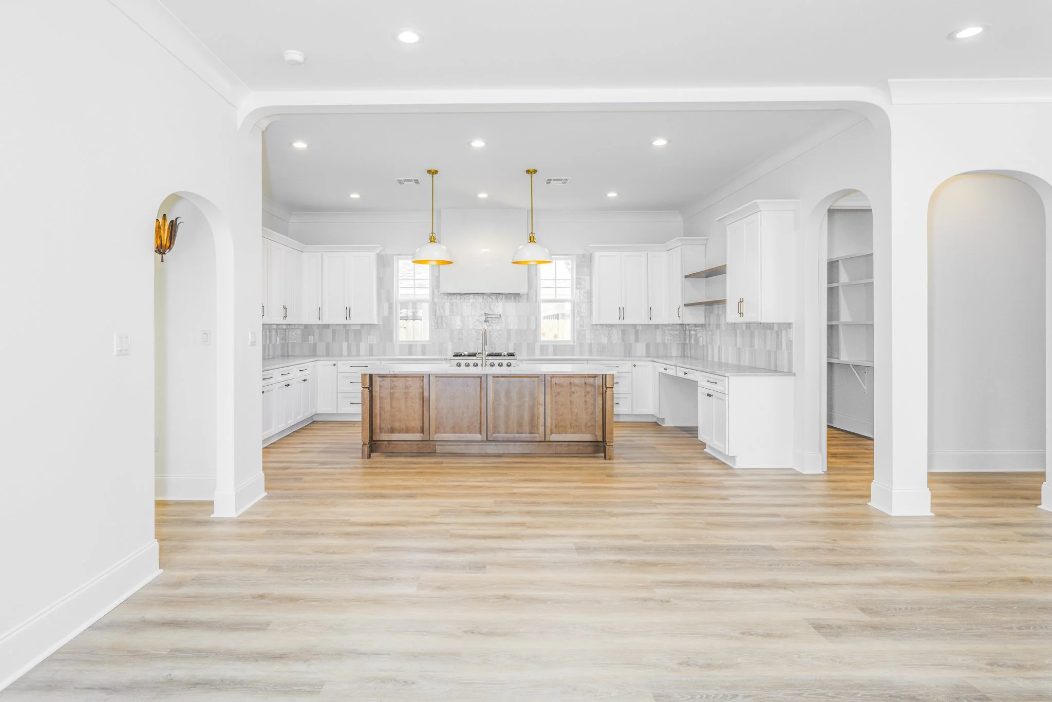 Open-concept kitchen with white cabinets, stainless steel appliances, pendant lighting, and wooden flooring.