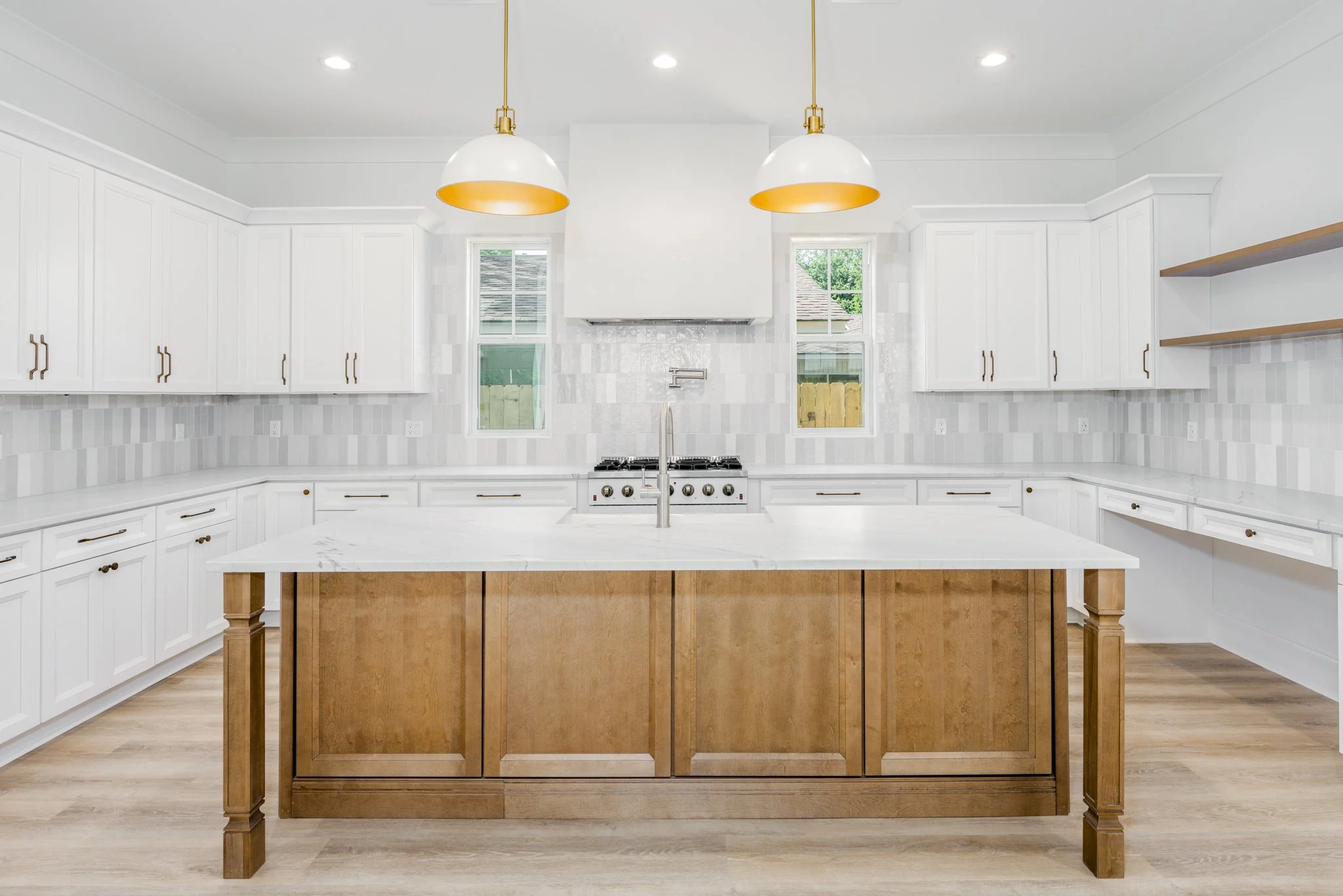 Modern kitchen with white cabinets, a marble island with a wooden base, and two hanging pendant lights with white and orange interiors.