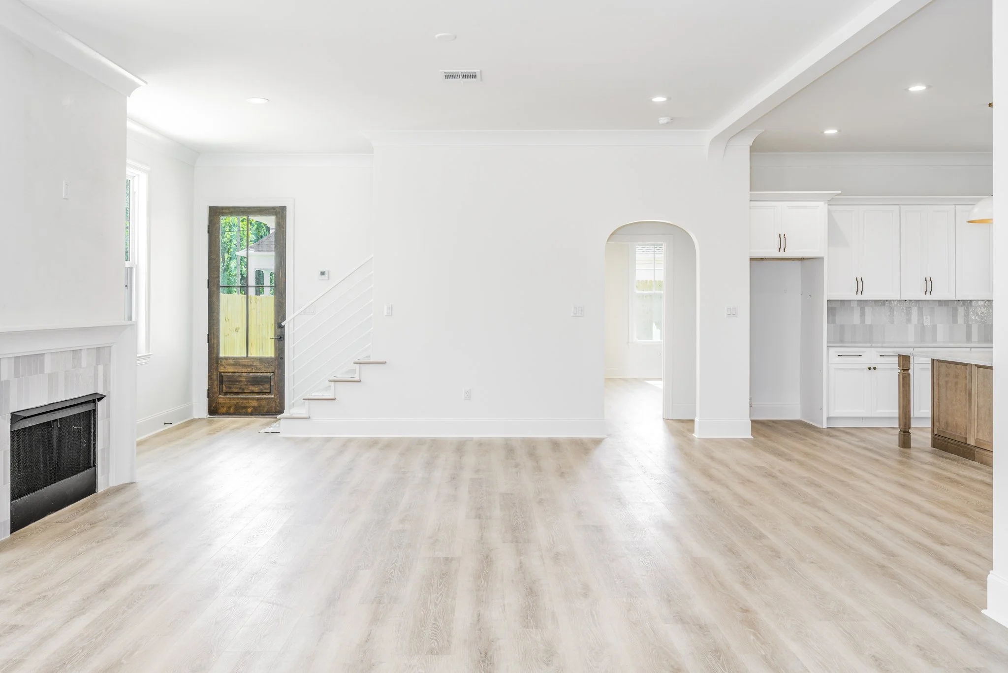 A spacious, bright, white kitchen and living area with hardwood floors, large windows, and a fireplace.