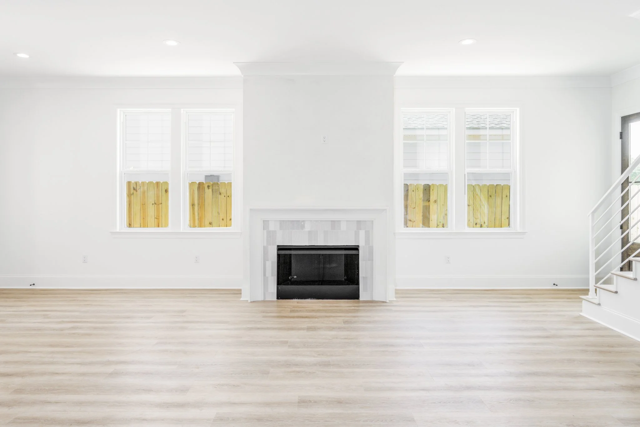 Living room with white walls, large windows with white shutters, a fireplace, and hardwood flooring.