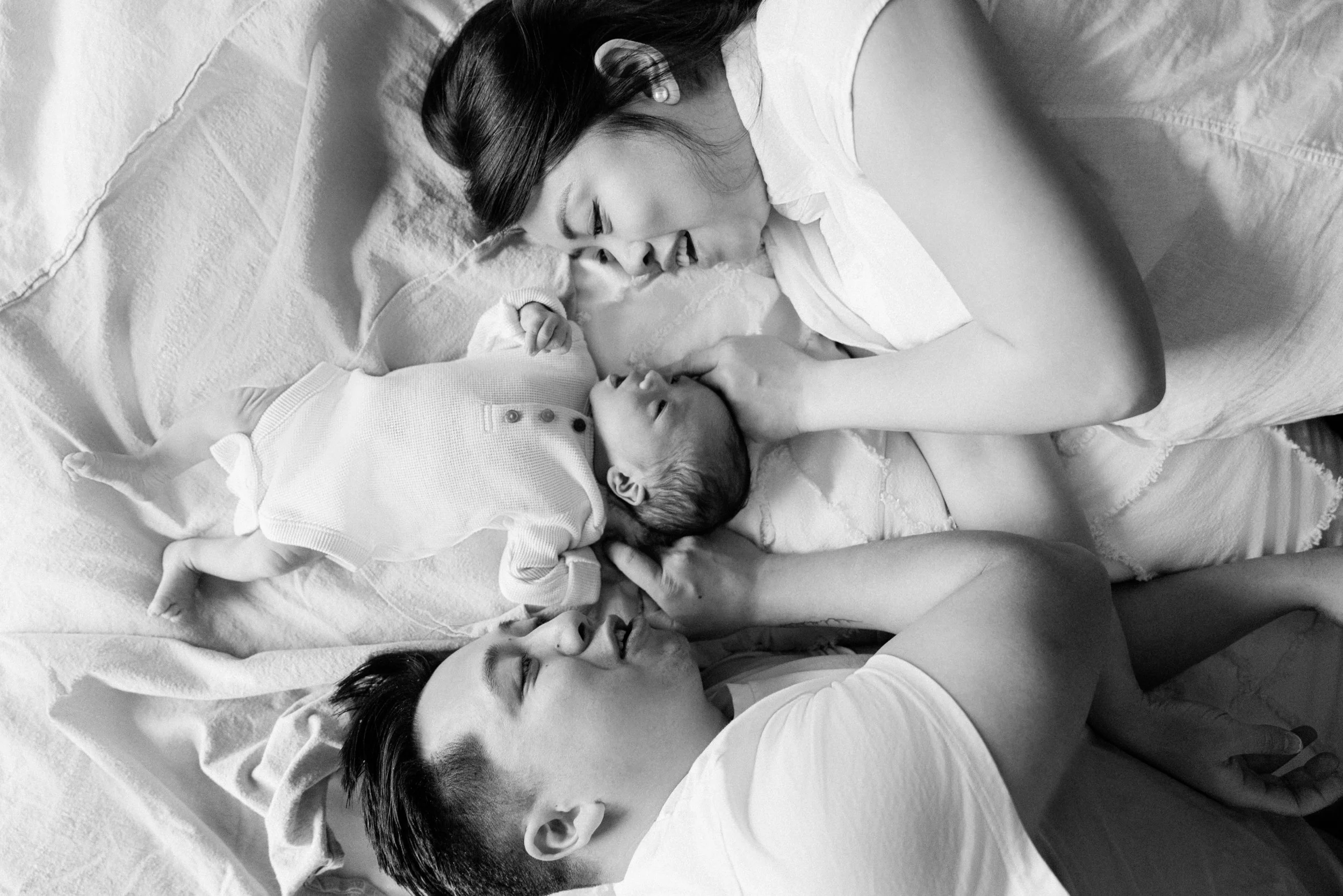 A woman and a man lying on a bed with a newborn baby, all breastfeeding and cuddling.