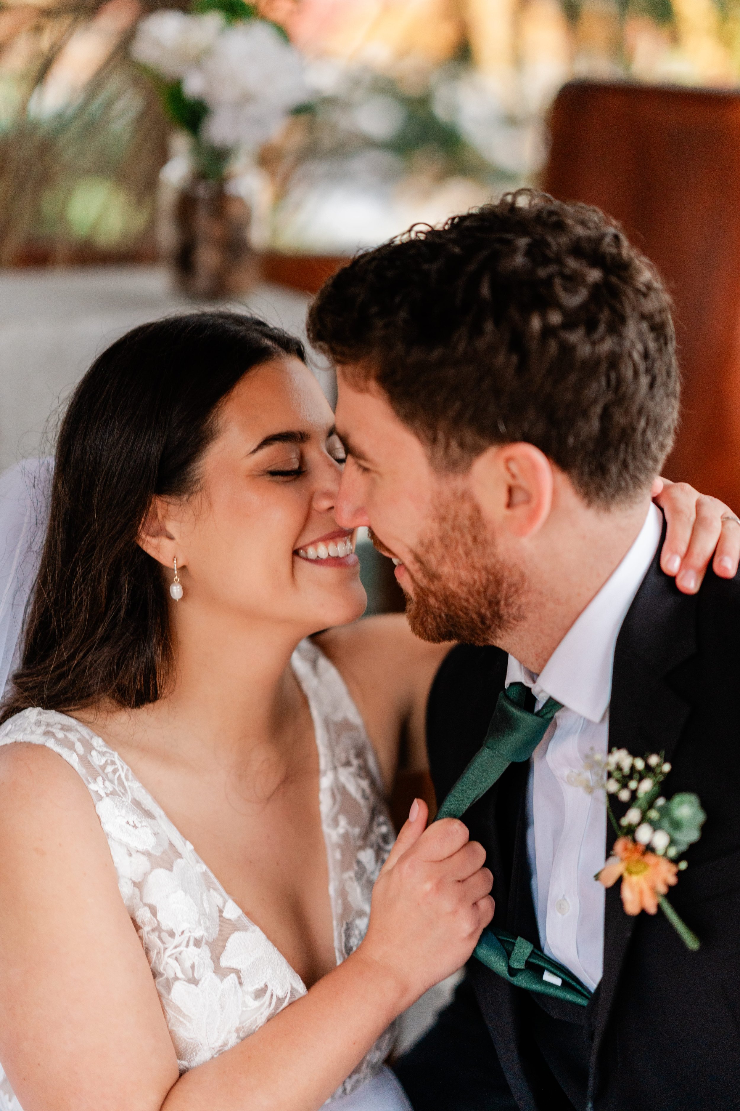 A bride and groom are close together, smiling, touching foreheads, and showing affection during their wedding celebration.