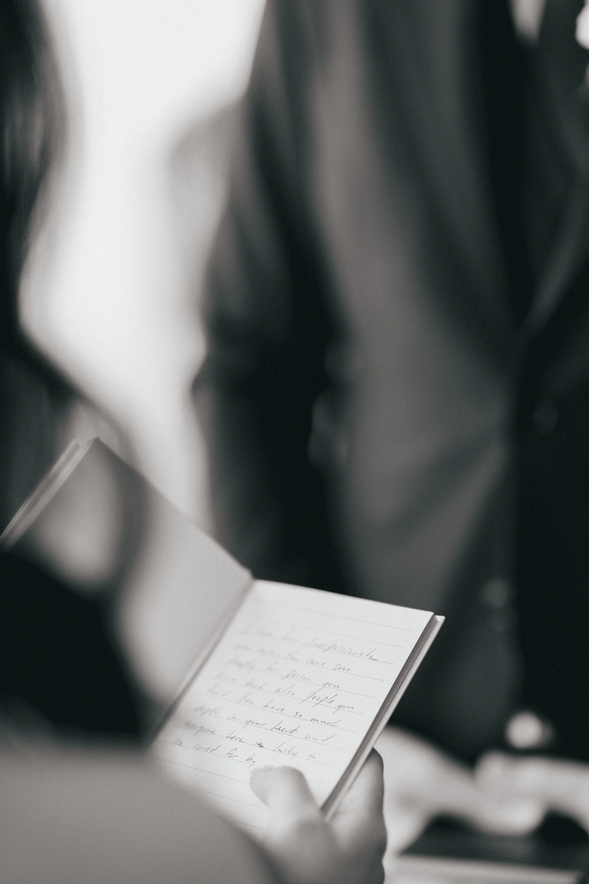 Person reading a handwritten note on a small open notebook, with other people in the background.