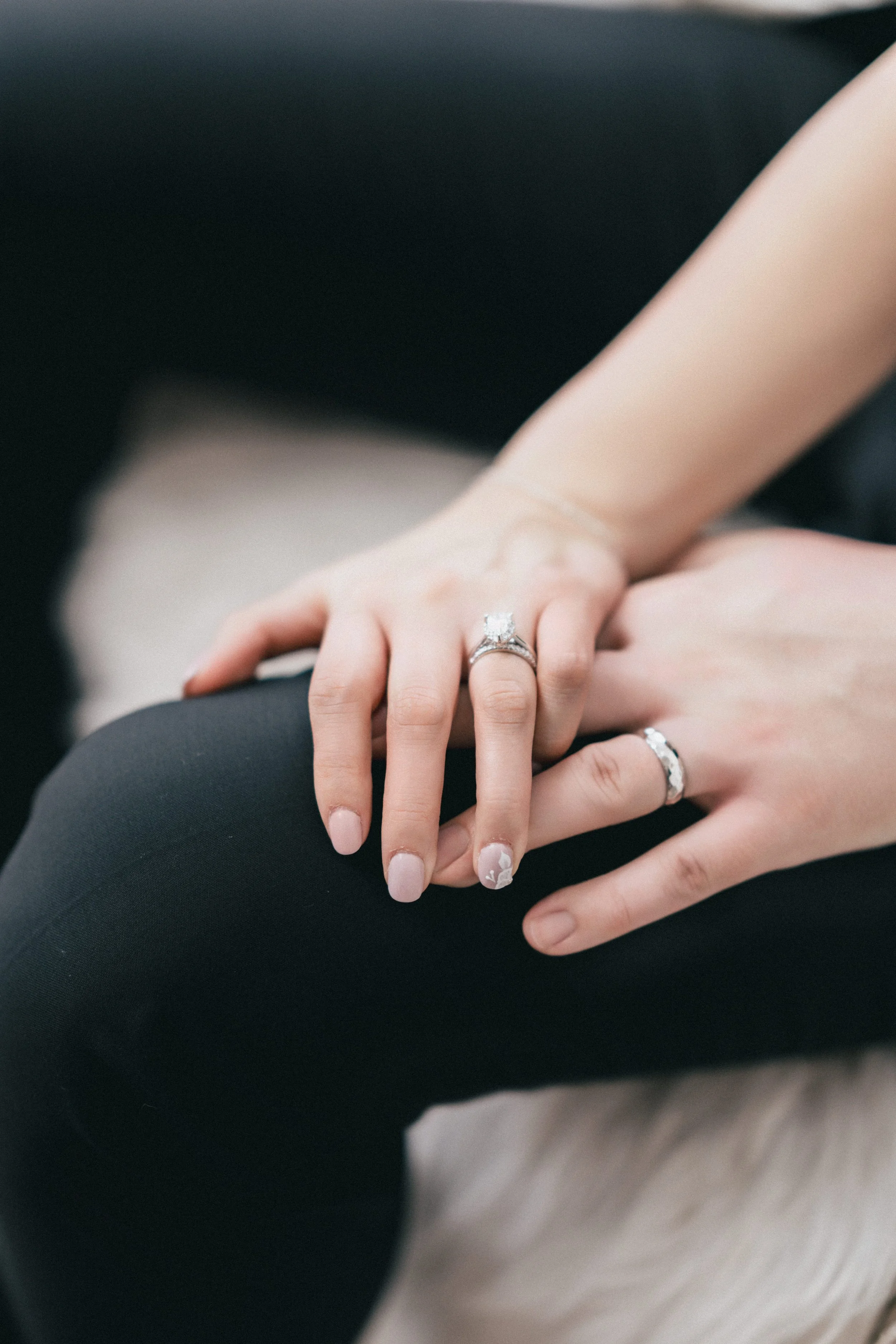 Close-up of a couple's hands with wedding rings, seated on a sofa.