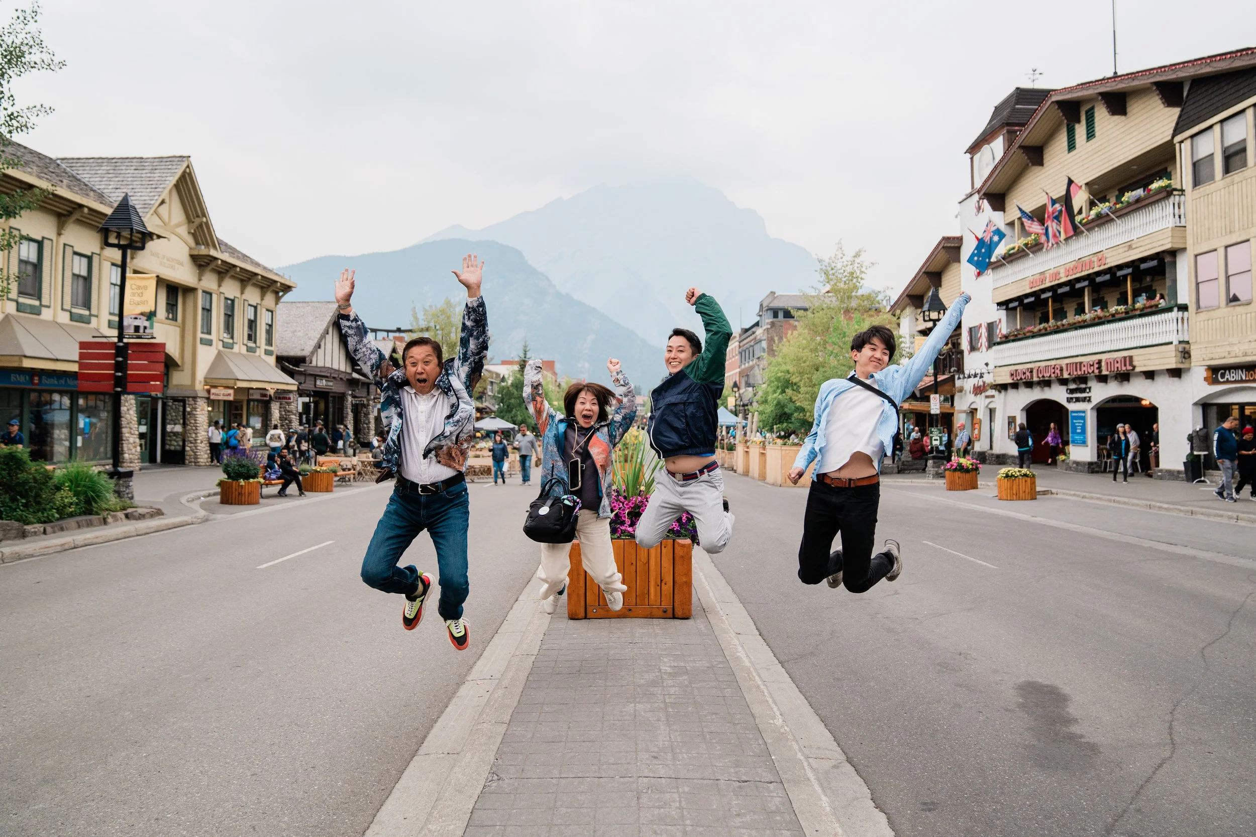 Four friends jumping in the air on a city street with buildings and mountains in the background.
