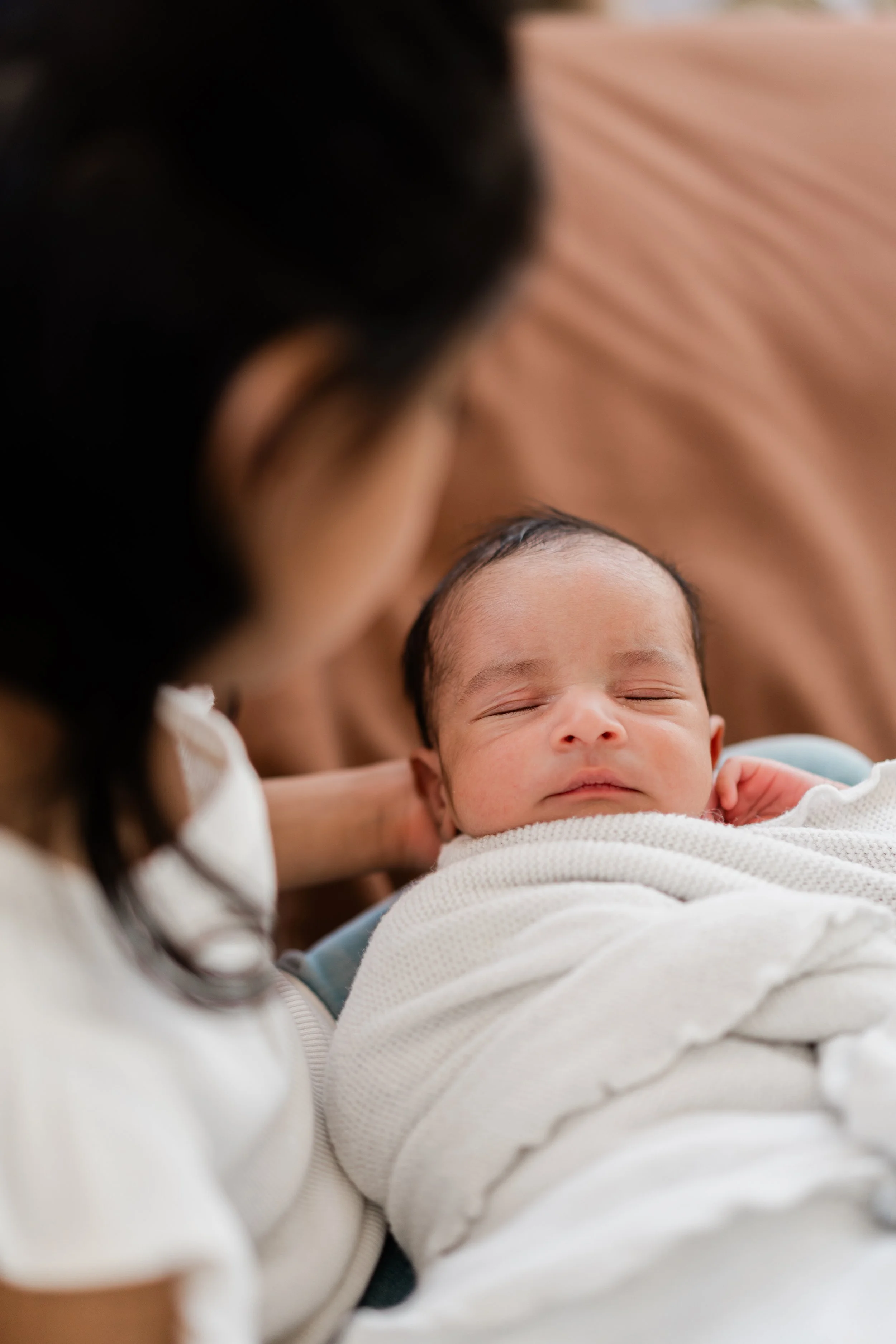 Close-up of a woman holding a sleeping baby on a bed.