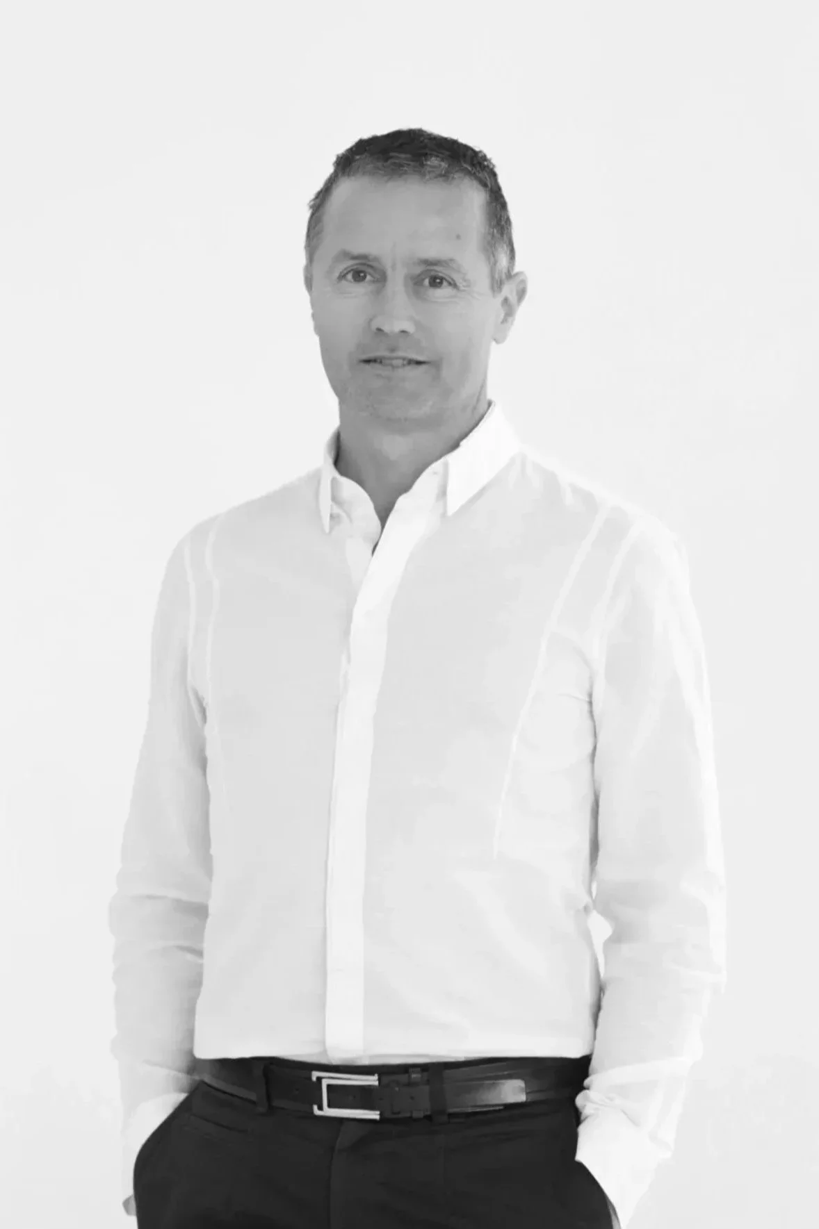 Black and white portrait of a man in a white dress shirt and black pants, standing against a plain background.