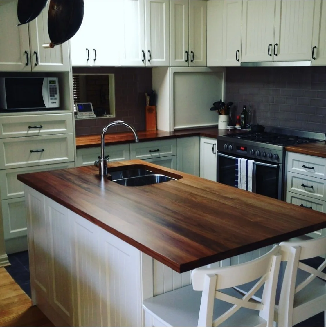 Modern kitchen with white cabinets, a wooden countertop, a black stove, a microwave, and a kitchen island with a sink.