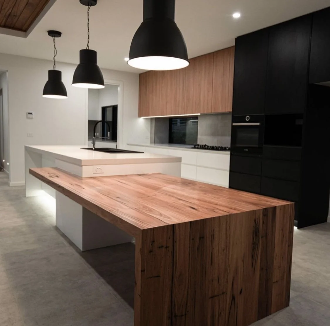 Modern kitchen with wooden and black cabinetry, white countertops, pendant lights, and a central island with a sink.
