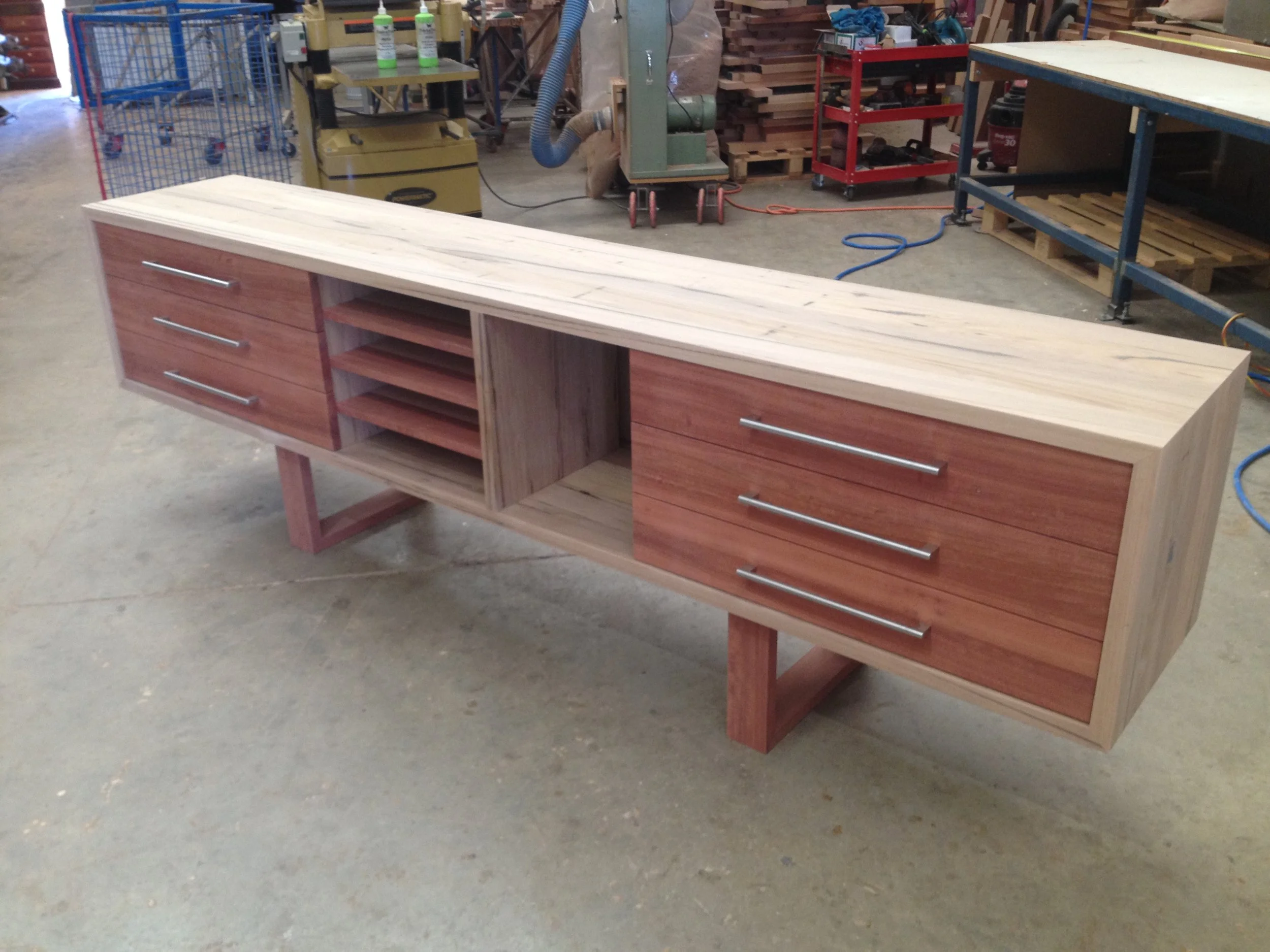 A wooden sideboard with drawers and open shelves in a woodworking shop.