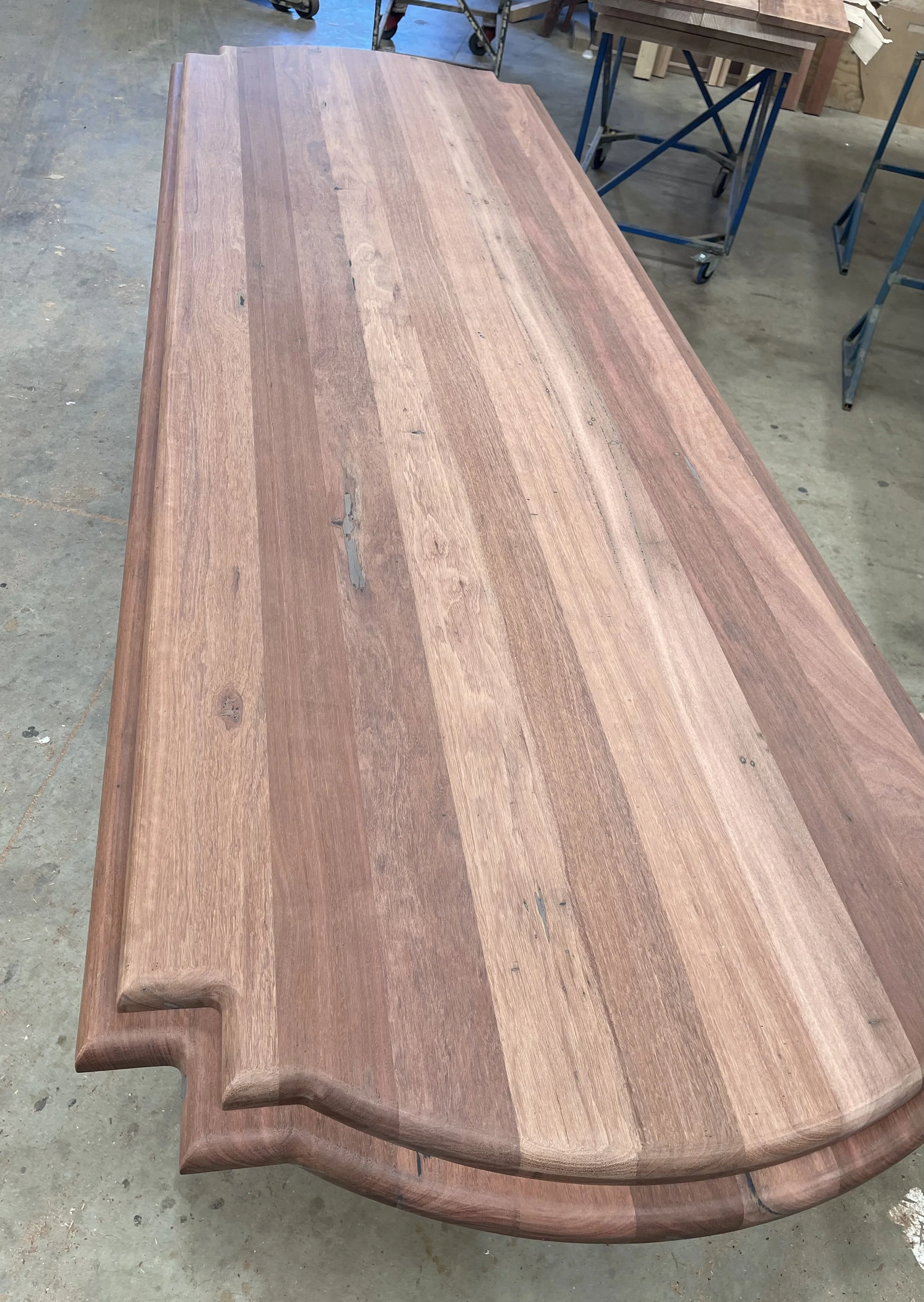 A large wooden workbench with a smooth, polished surface and rounded edges in a workshop setting.